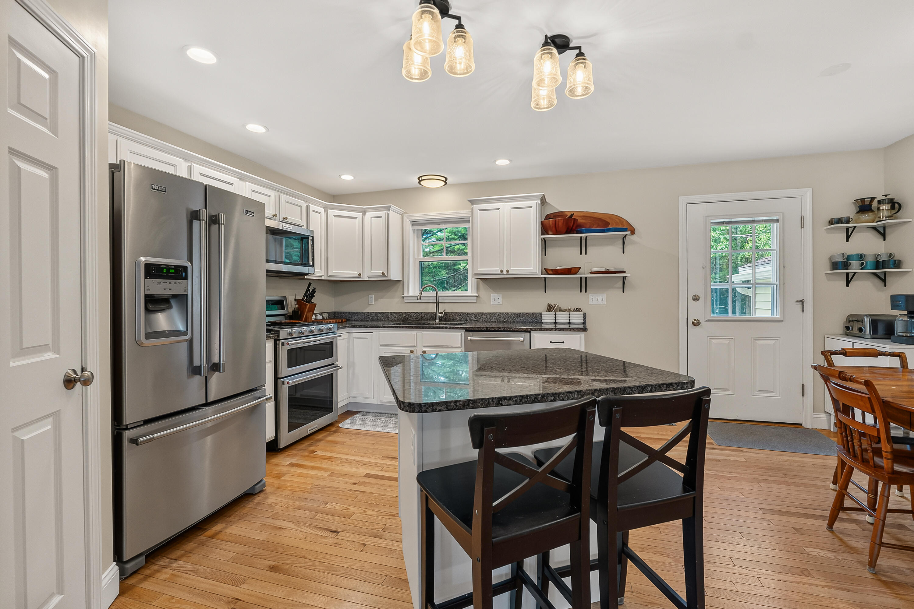 Kitchen with white cabinets, stainless steel appliances, granite island, and hardwood floors.