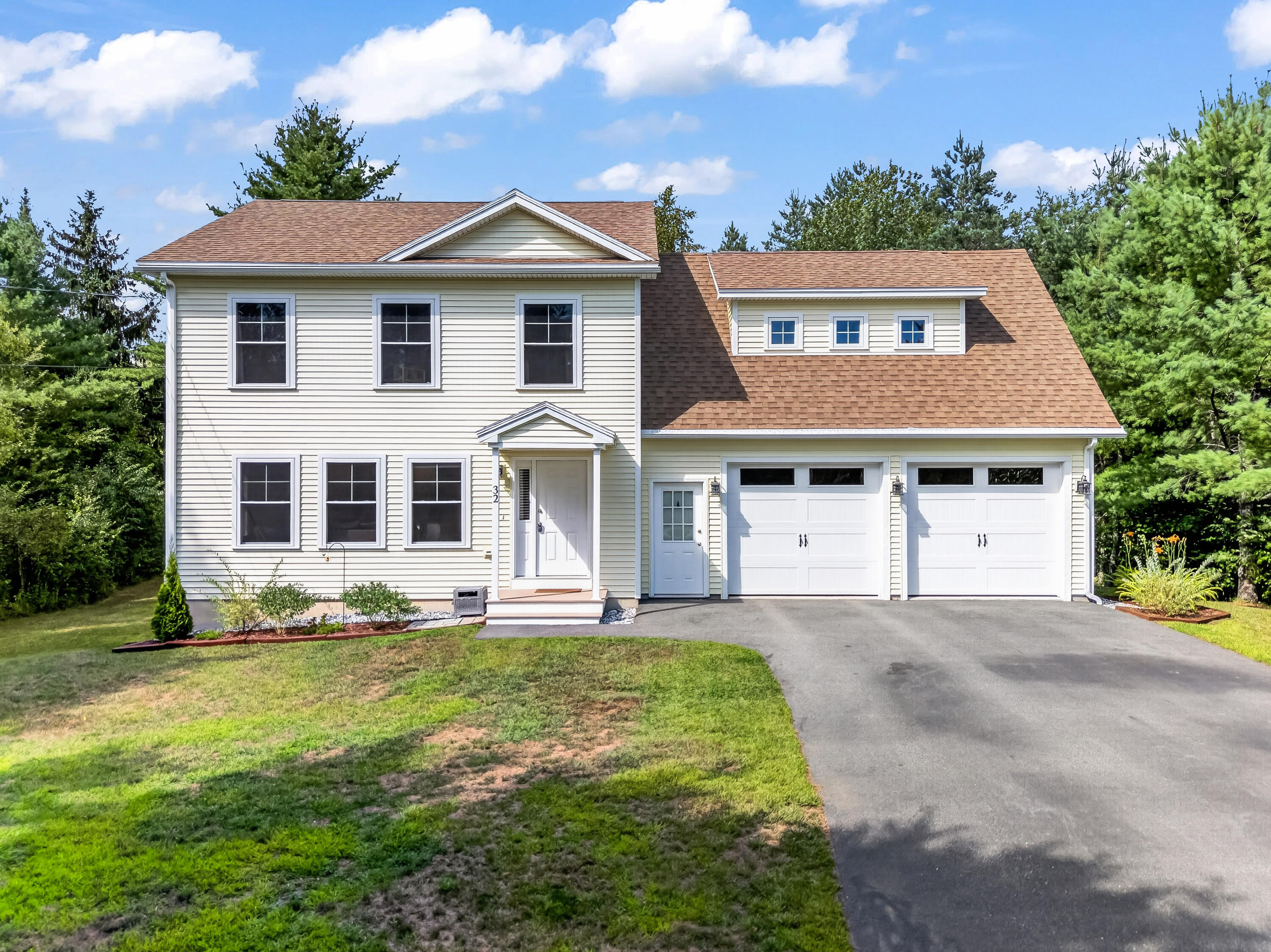 Two-story cream house with a brown roof, two-car garage, and paved driveway.
