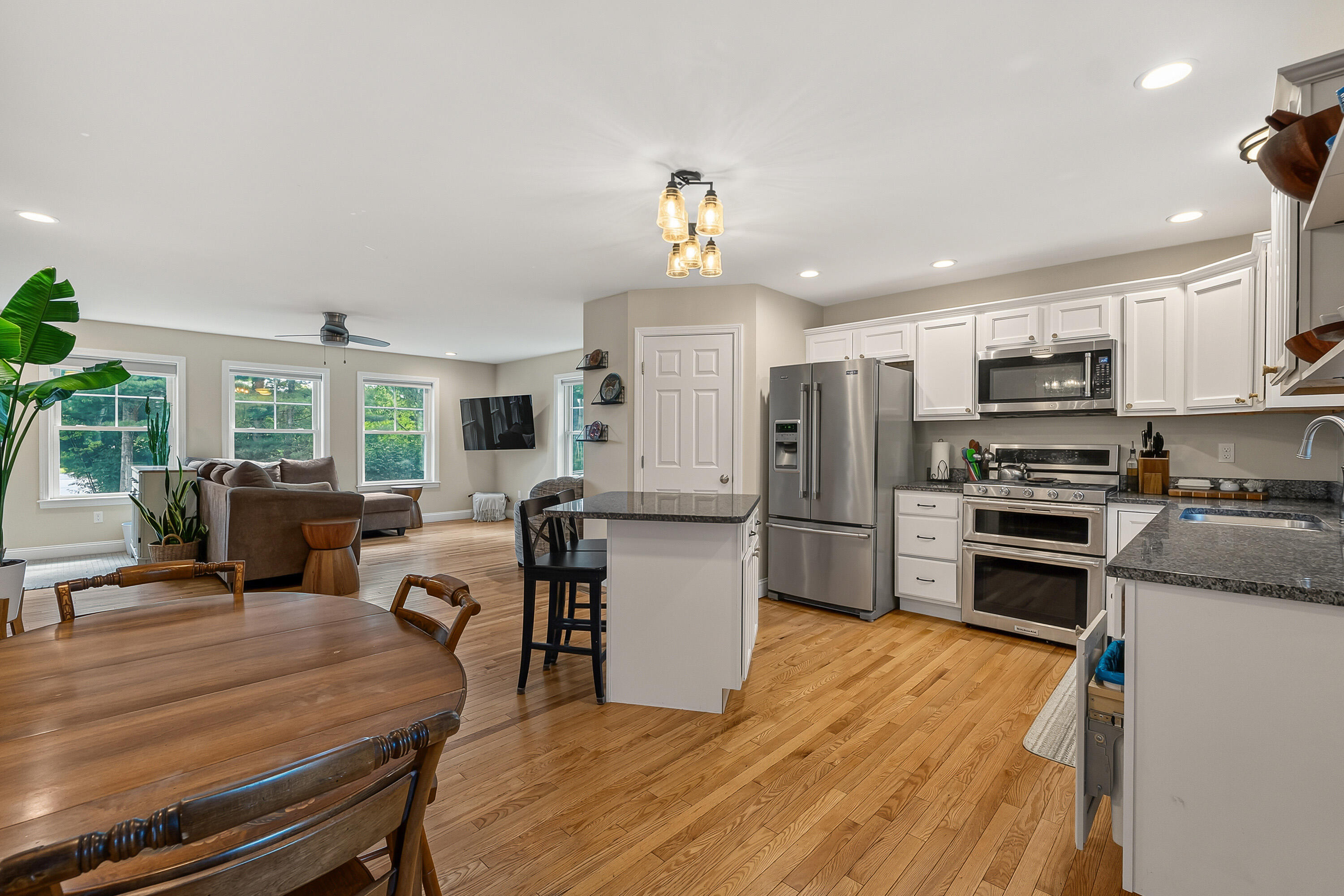 Open-plan kitchen with stainless steel appliances and island beside a hardwood-floored living and dining area.