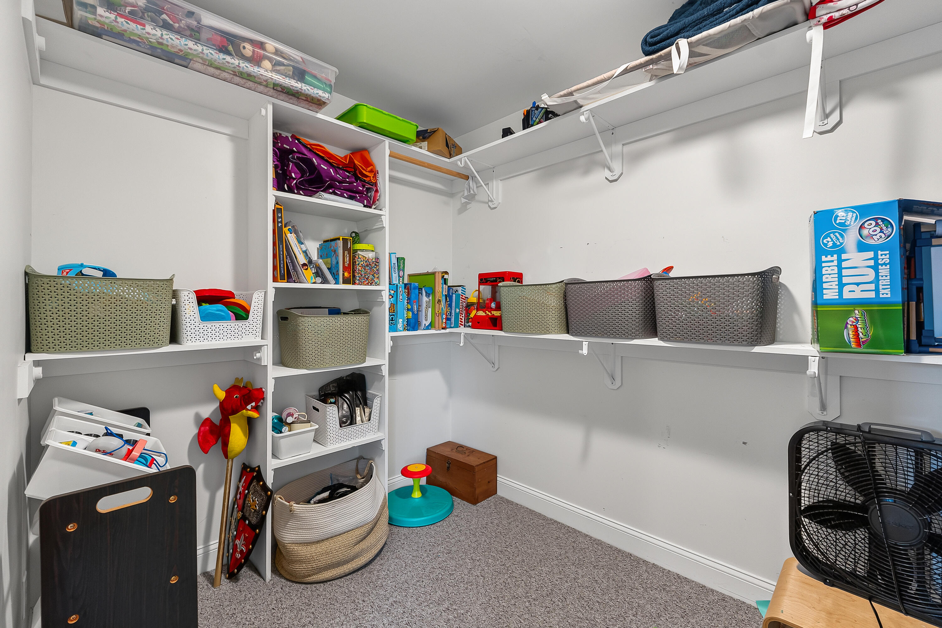 Carpeted storage room with wraparound shelves, toy-filled baskets, and a large Marble Run box.