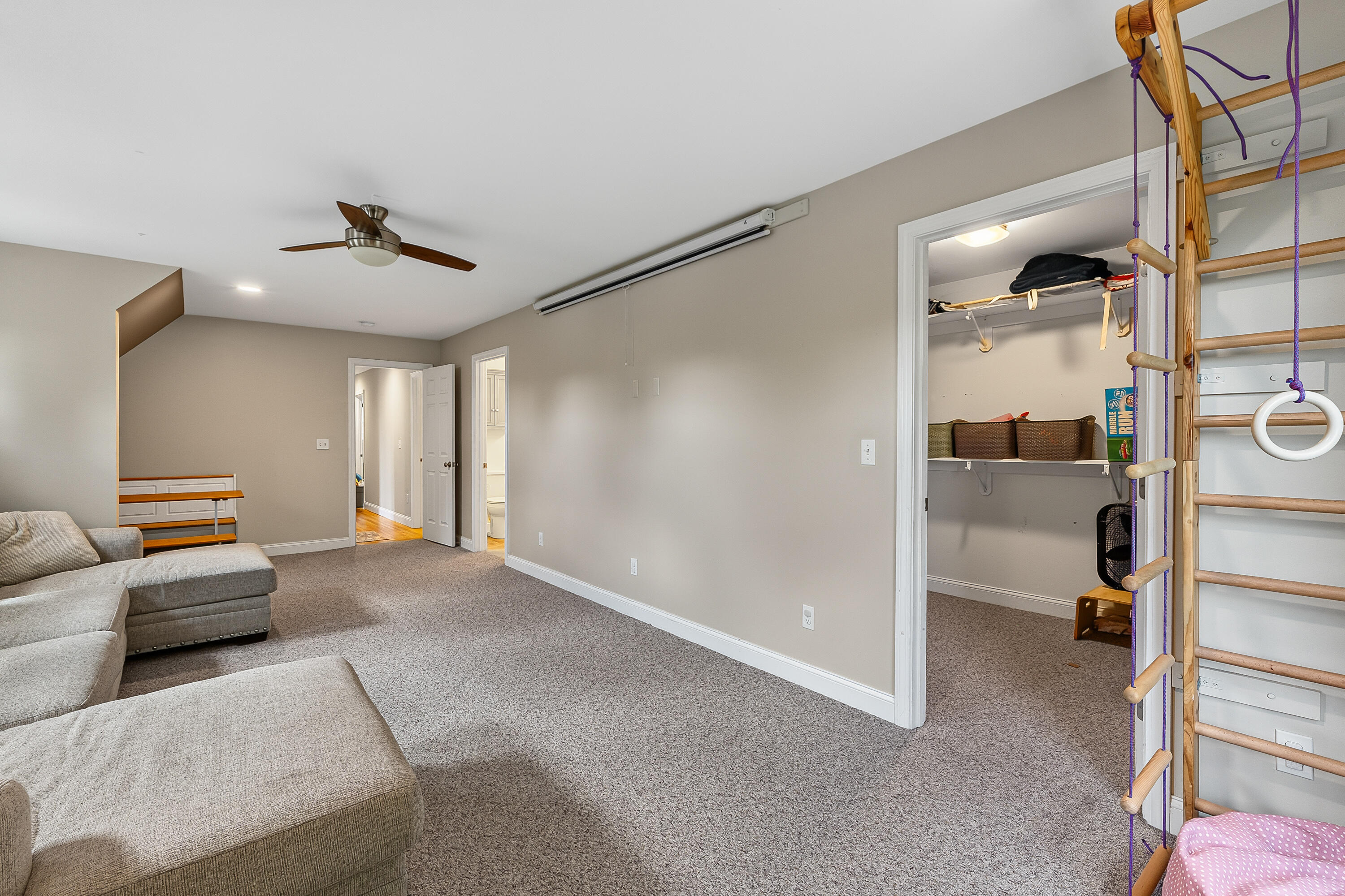 Carpeted bonus room with a gray sectional sofa and a wooden climbing ladder with ropes and gym rings.