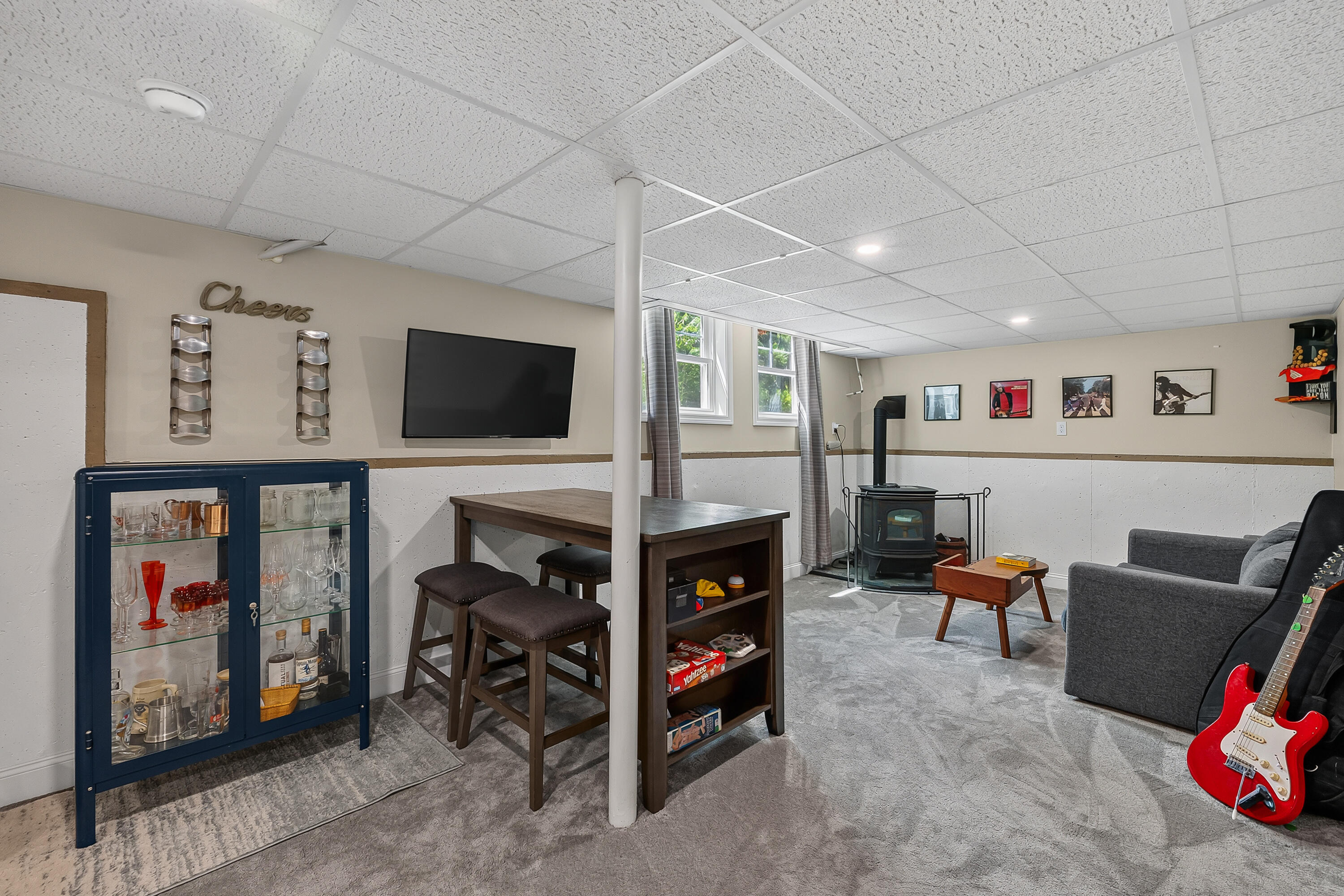 Basement recreation room with a game table, bar cabinet, wood stove, and red electric guitar.