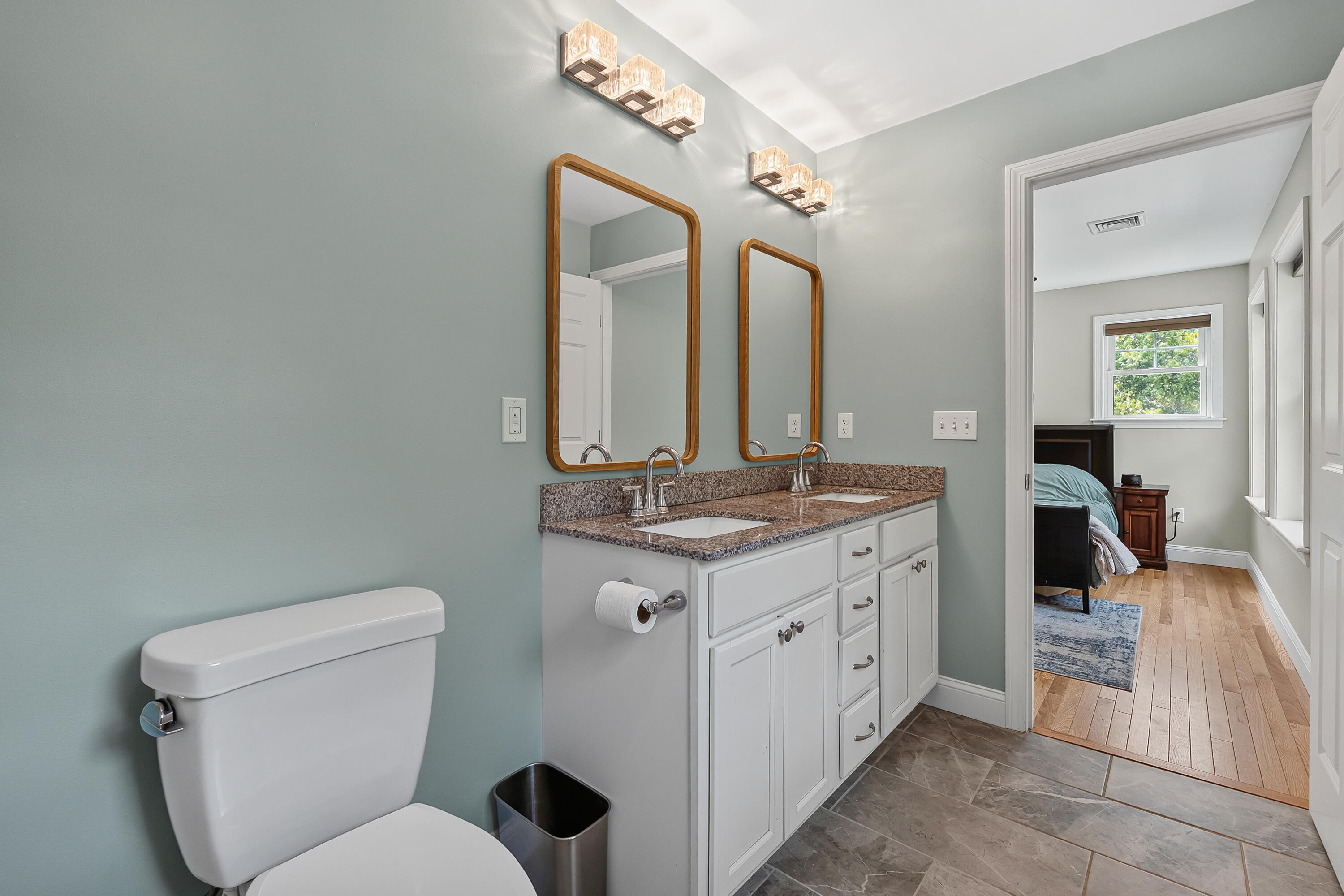 Bathroom with double vanity and wood-framed mirrors, opening onto a bedroom.