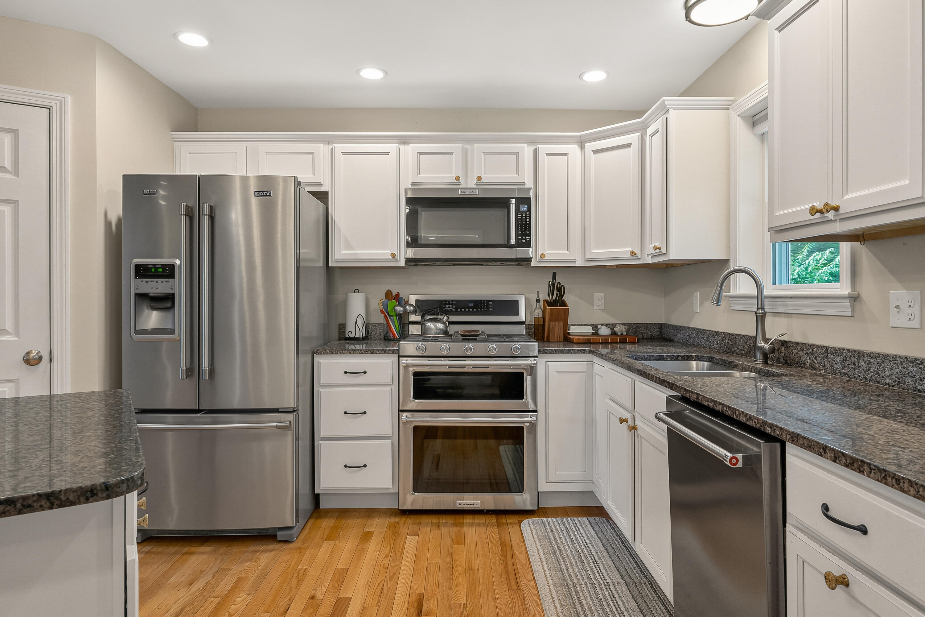 Kitchen with white cabinets, granite counters, stainless appliances, and hardwood floors.