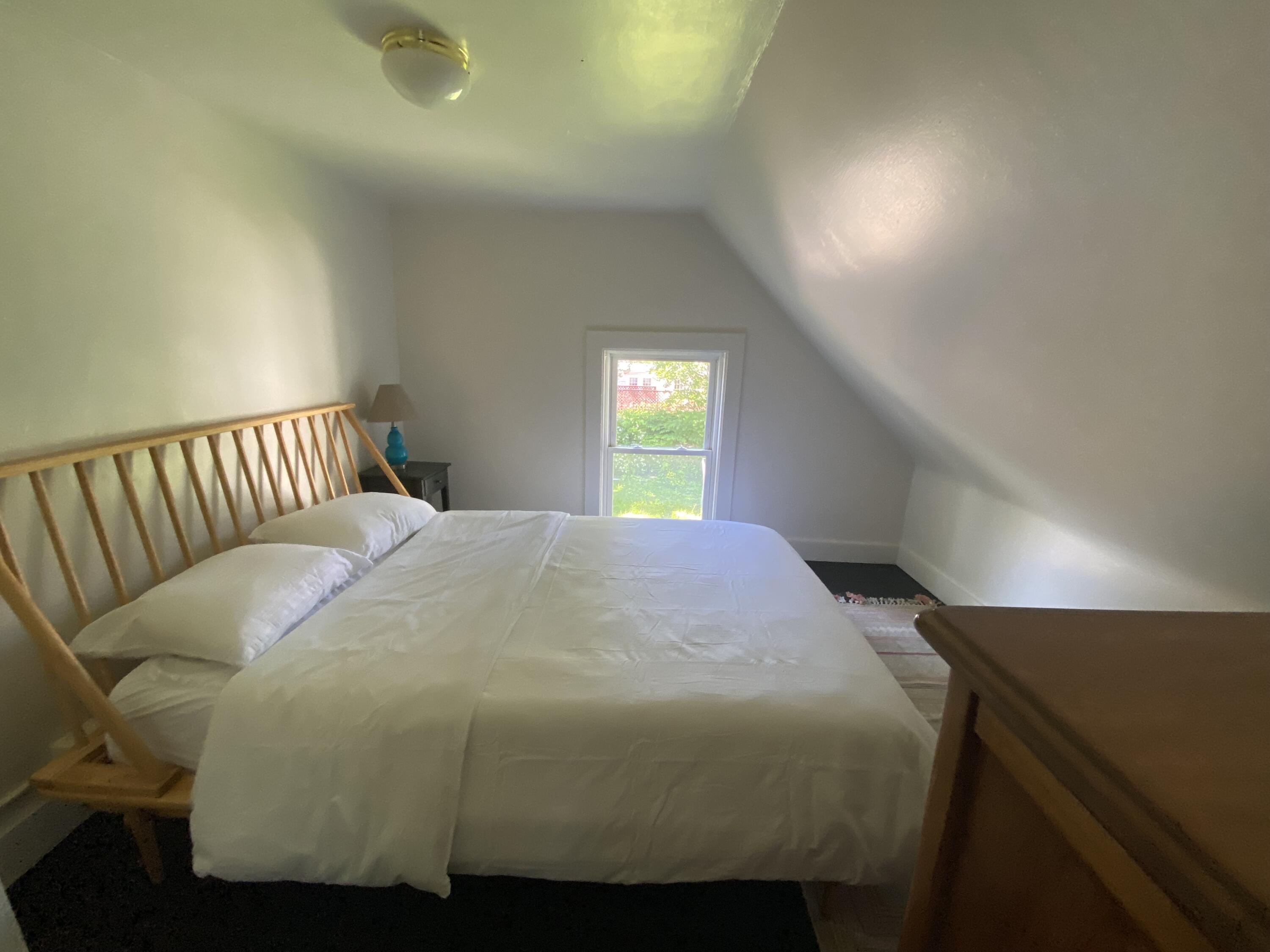 Furnished bedroom with a white bed, light wood spindle headboard, and sloped ceiling.