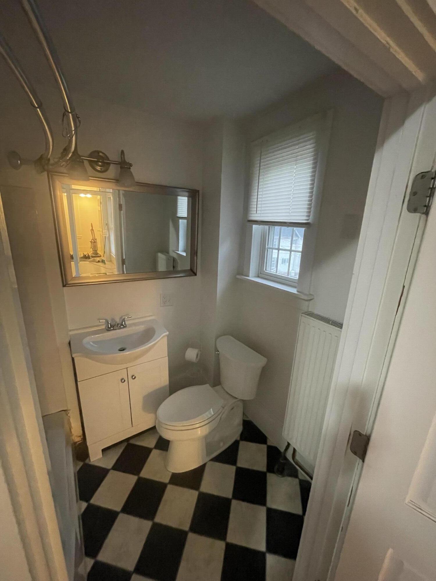 Bathroom with a sink, toilet, window, radiator, and black-and-white checkerboard floor.
