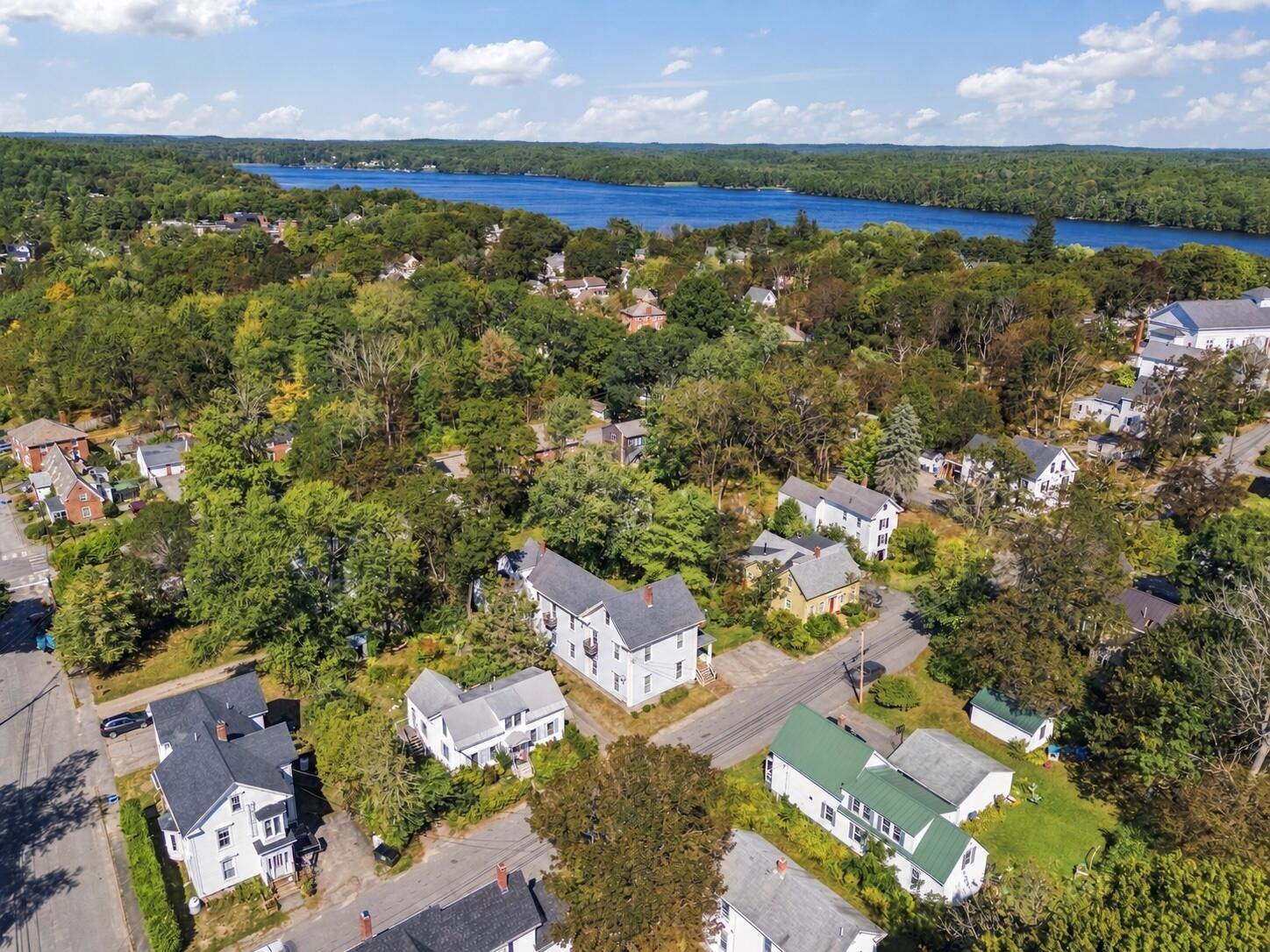 Aerial view of a leafy neighborhood, with homes in the foreground and a wooded shoreline across the water.