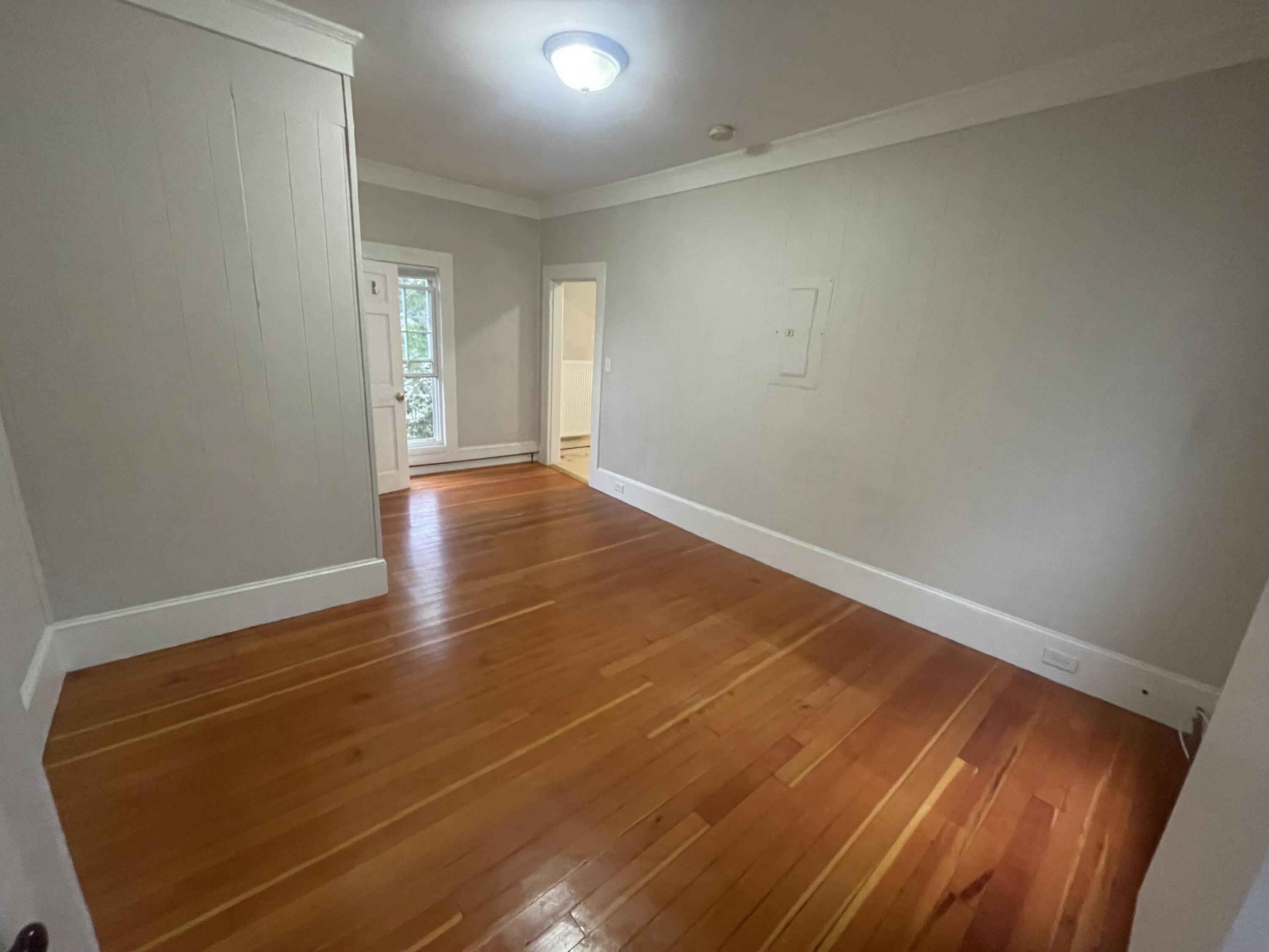 Empty room with polished hardwood floors, gray walls, and a tall window beside a doorway.