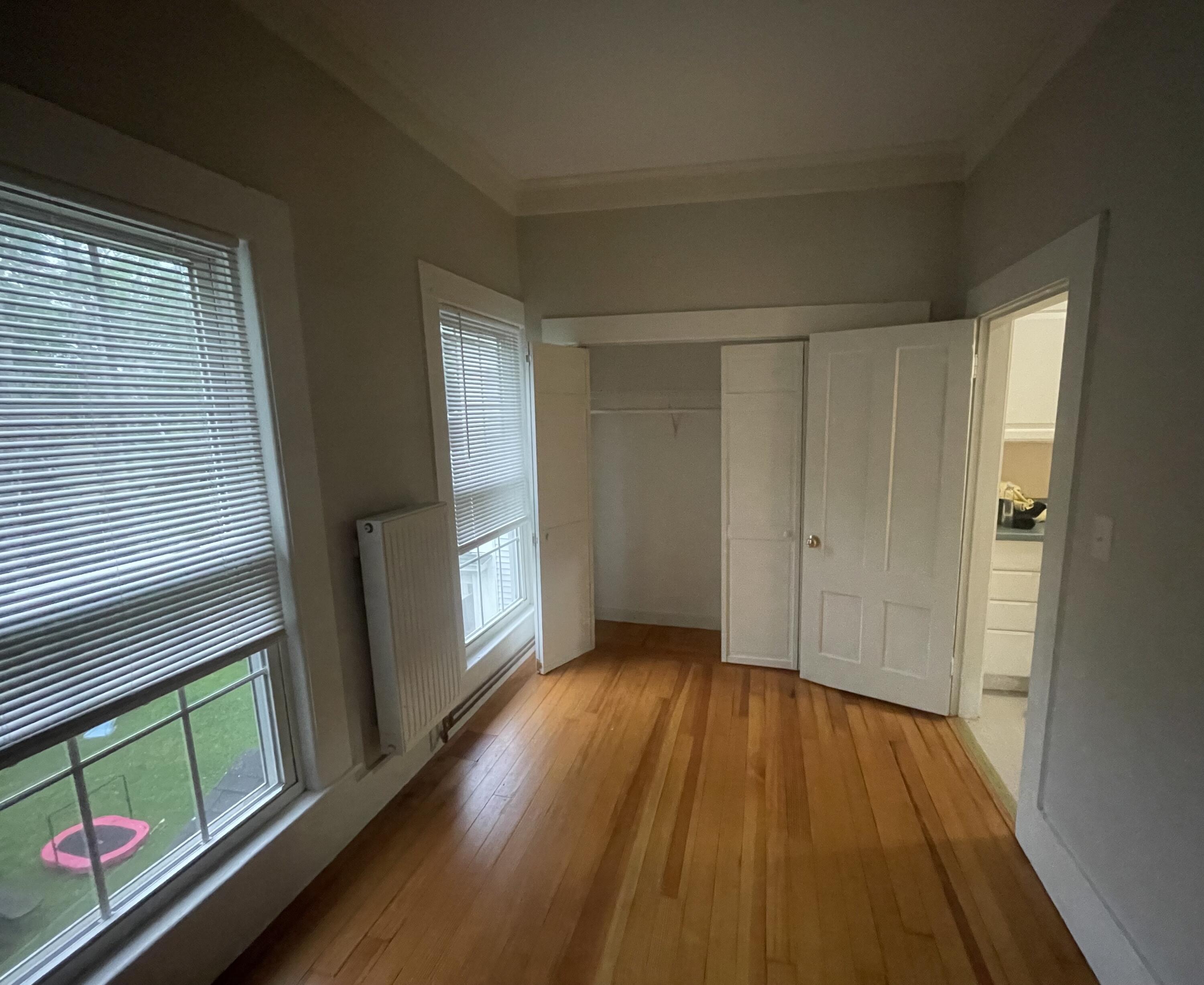 Unfurnished room with hardwood floors, two blind-covered windows, a radiator, and an open closet.