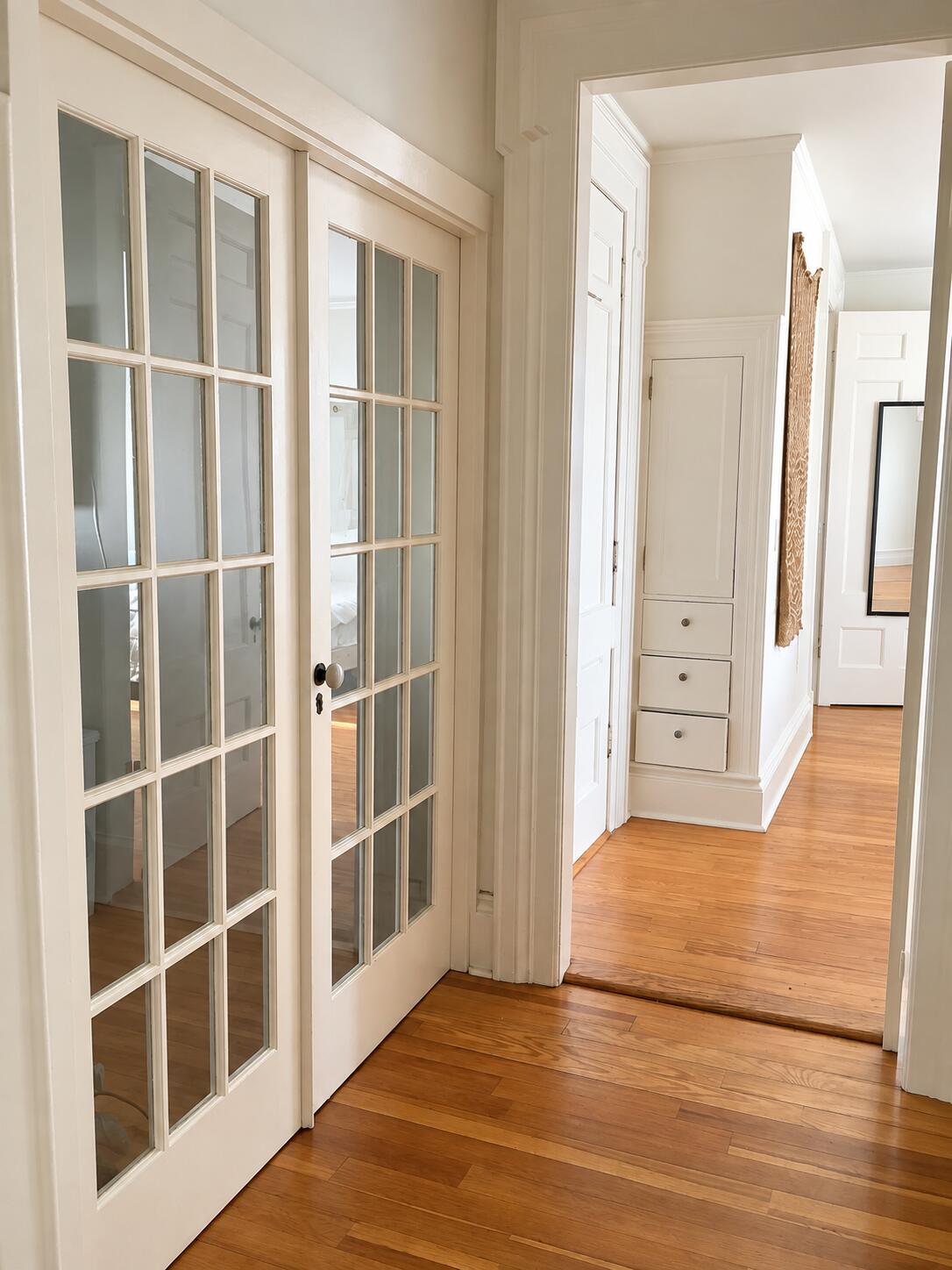 Hallway with glass-paneled French doors, hardwood floors, and built-in drawers.