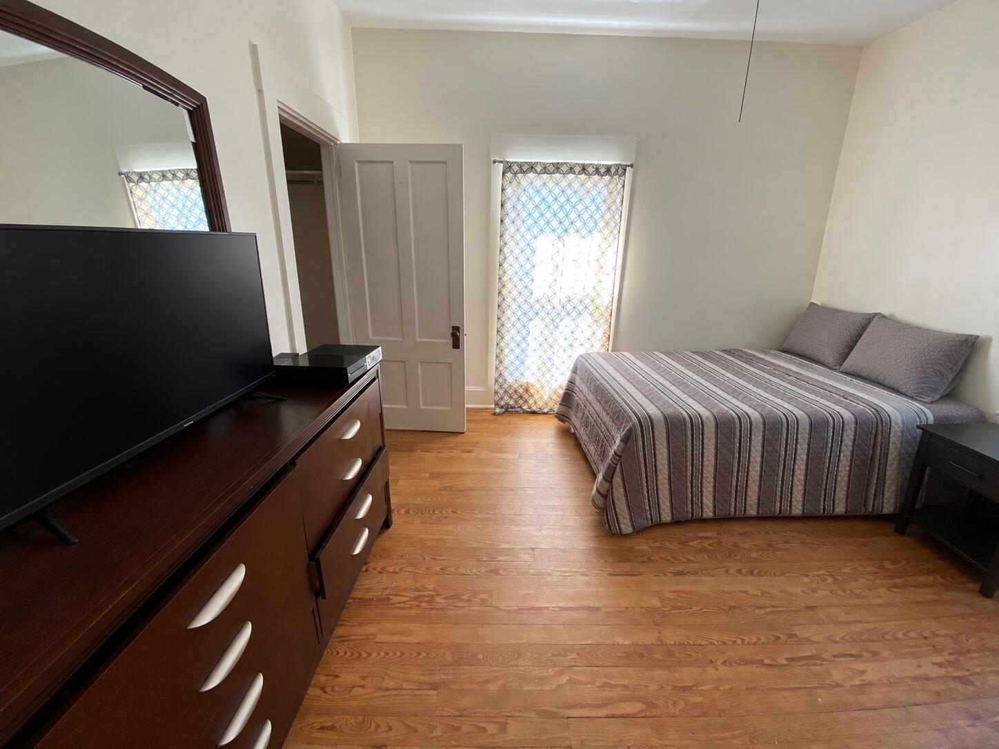 Bedroom with a gray striped bedspread, hardwood floors, and a dark wooden dresser with television.