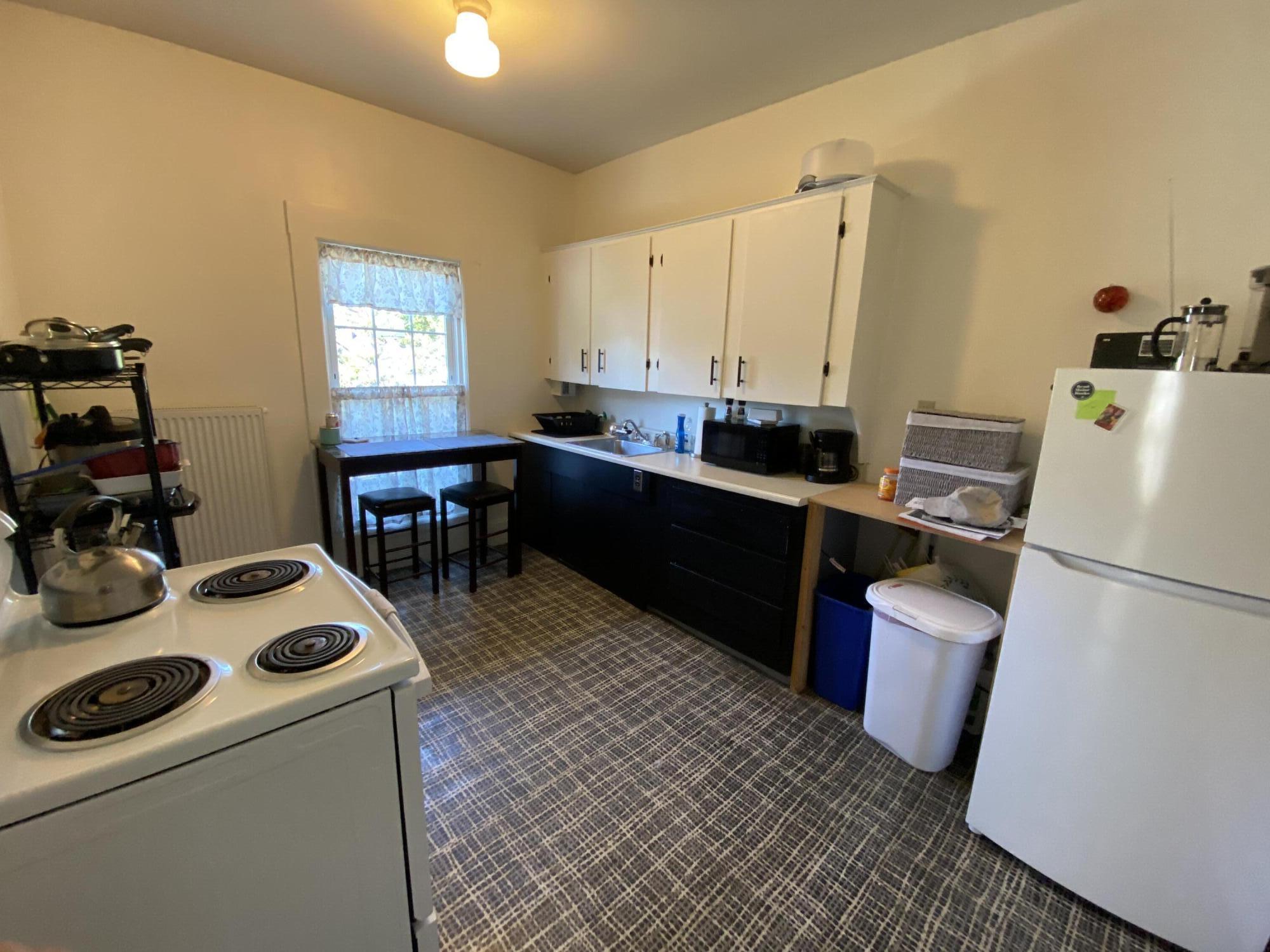 Kitchen with black lower cabinets, white upper cabinets, and a small table by the window.