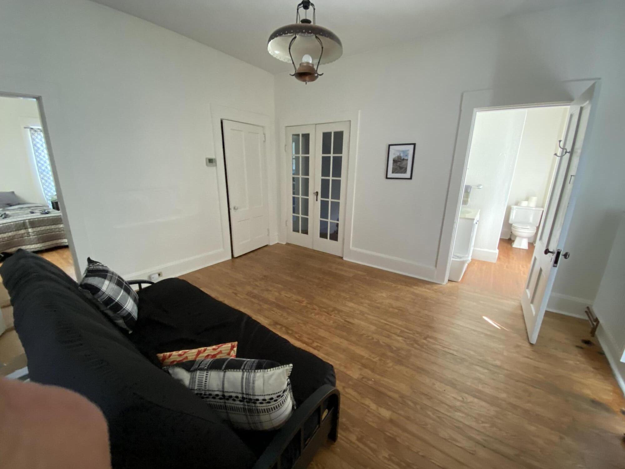 Living room with hardwood floors, a black sofa, French doors, and a bathroom doorway.
