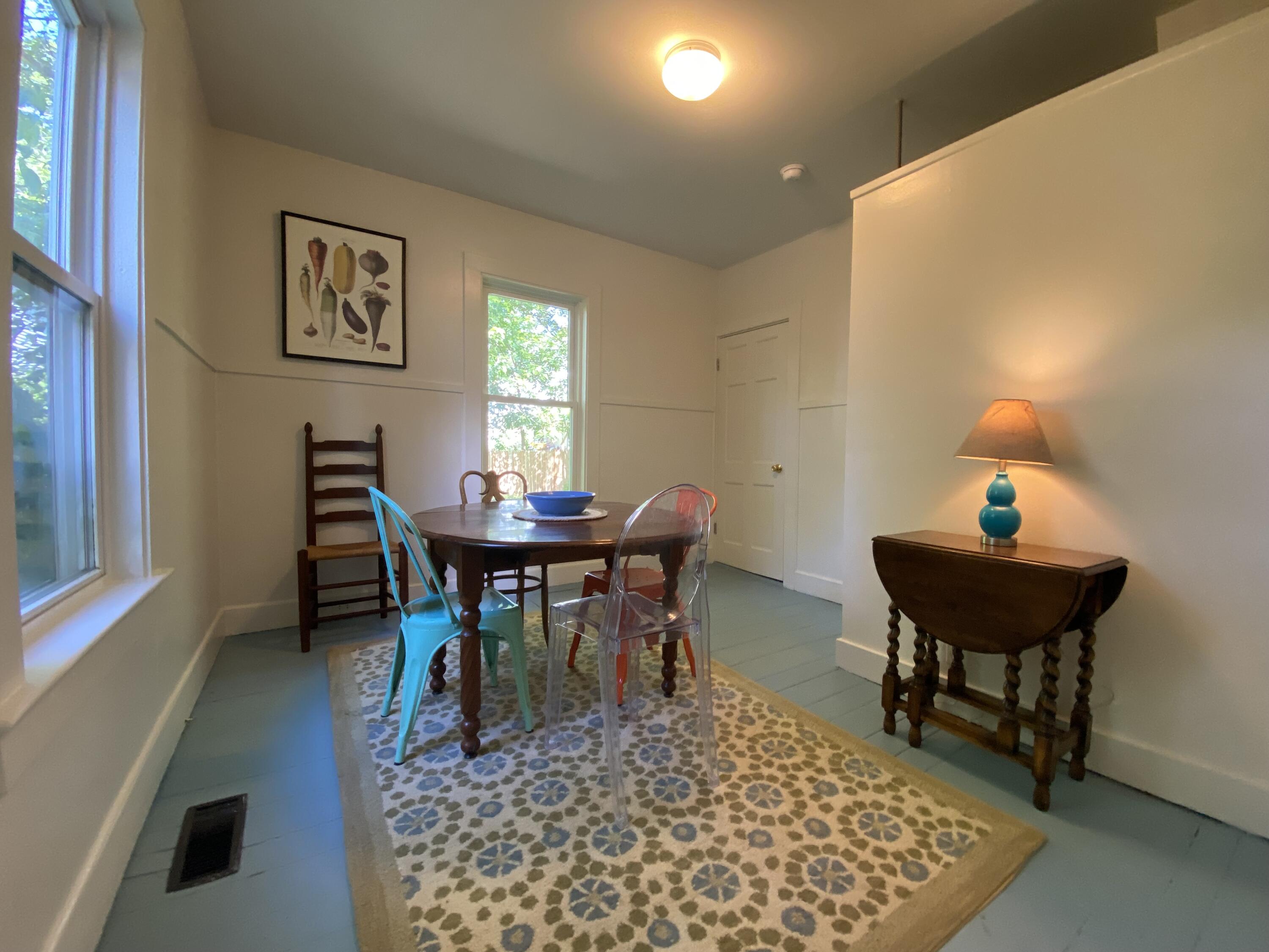 Dining room with a round table, colorful chairs, blue floorboards, and a patterned rug.