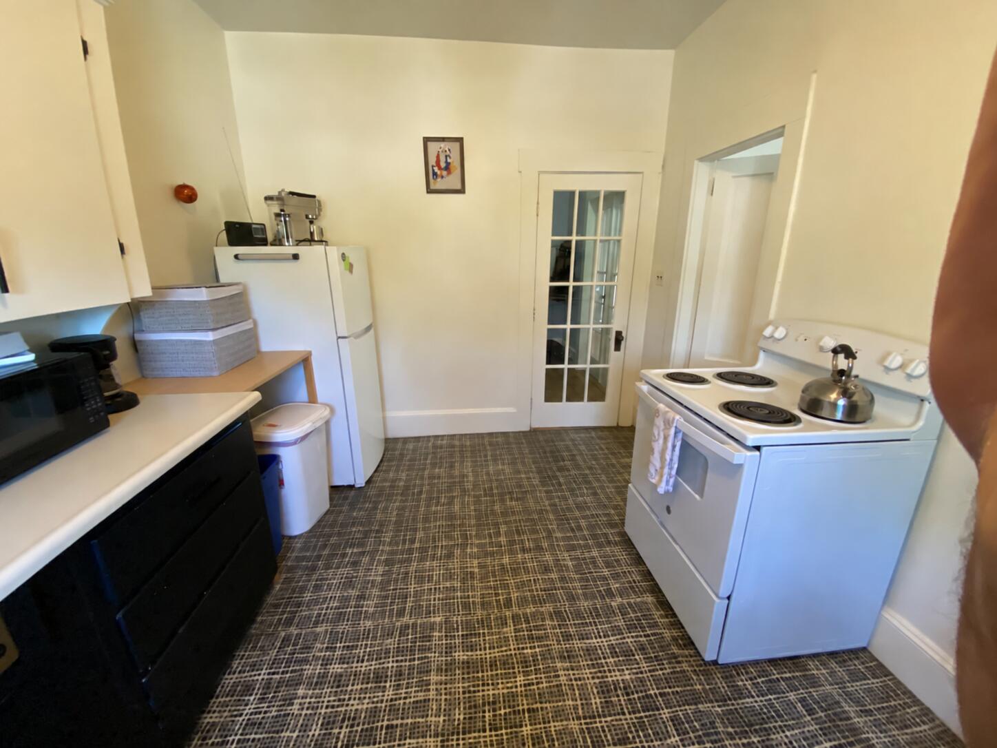 Compact kitchen with a white electric range, refrigerator, and dark patterned flooring.