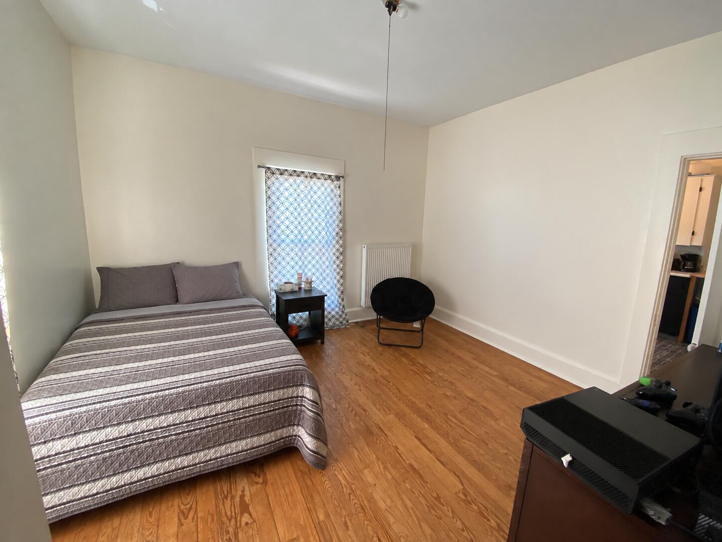 Bedroom with a gray striped bedspread, hardwood floors, and a black accent chair.