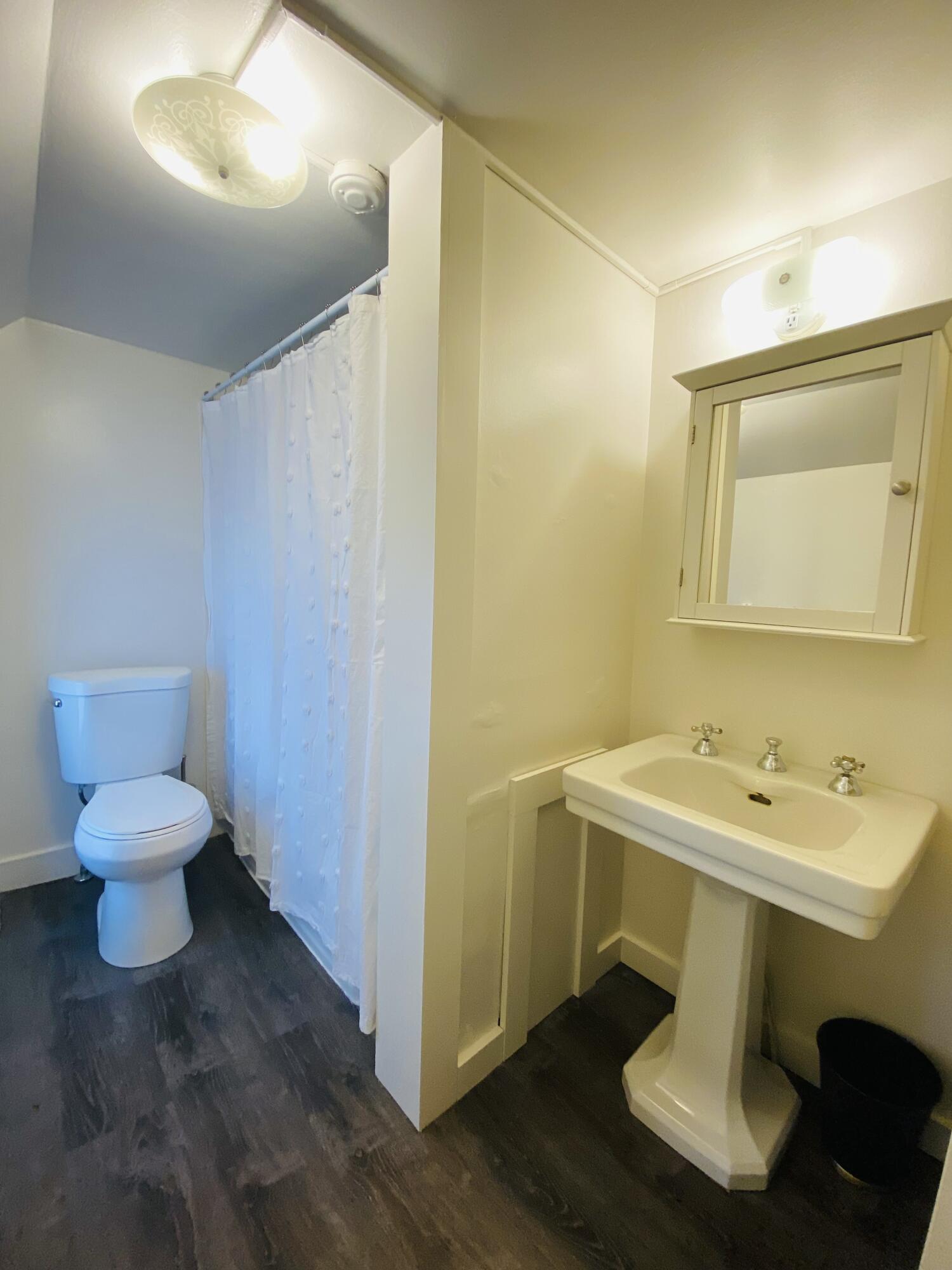 Bathroom with pedestal sink and mirrored cabinet beside a toilet and curtained shower.