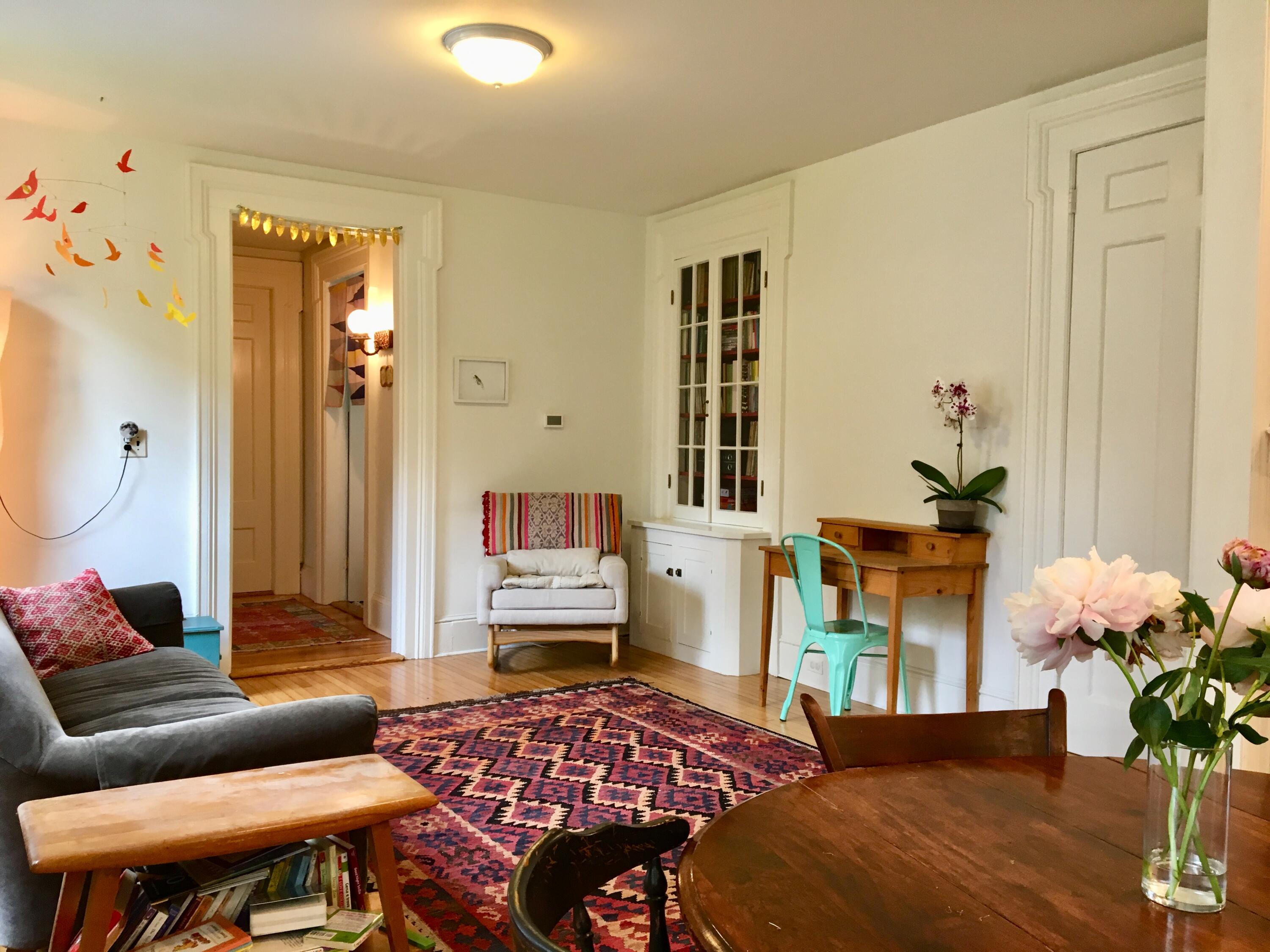Furnished living room with a patterned rug, built-in glass-front bookcase, and turquoise desk chair.