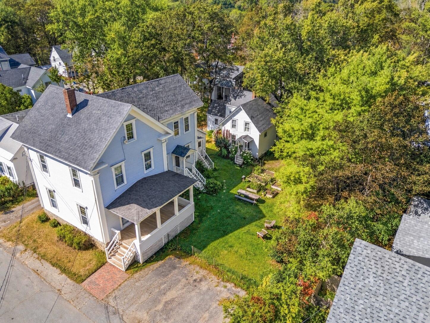 Aerial view of a blue-and-white multi-unit house with porches and a leafy shared yard.