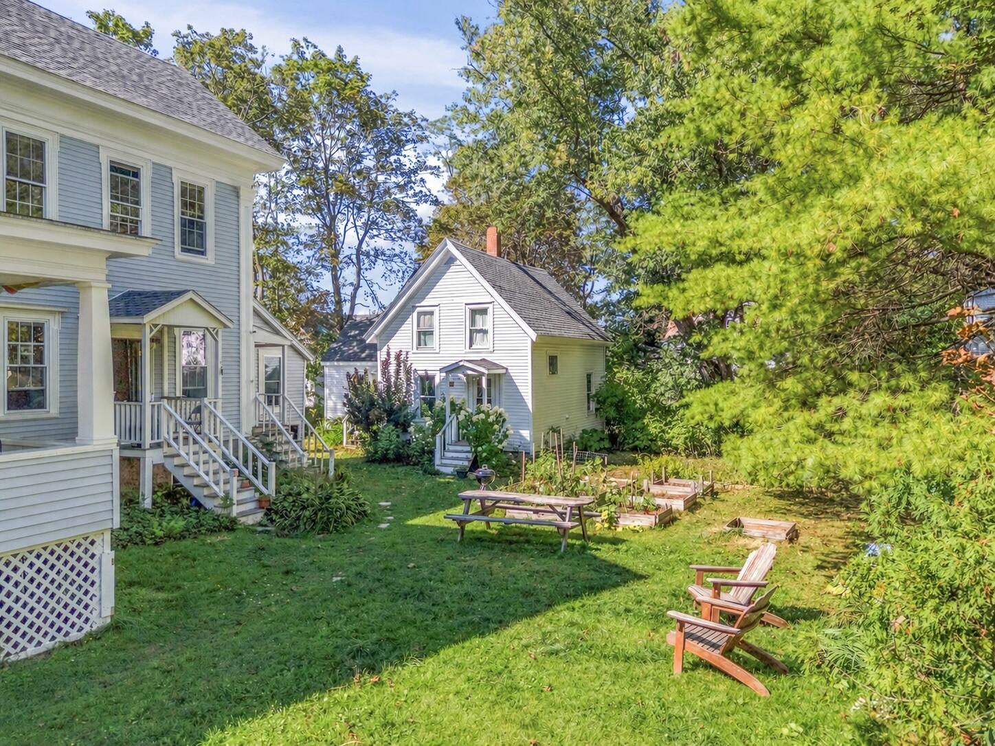 Backyard between two houses with a lawn, picnic table, garden beds, and leafy trees.