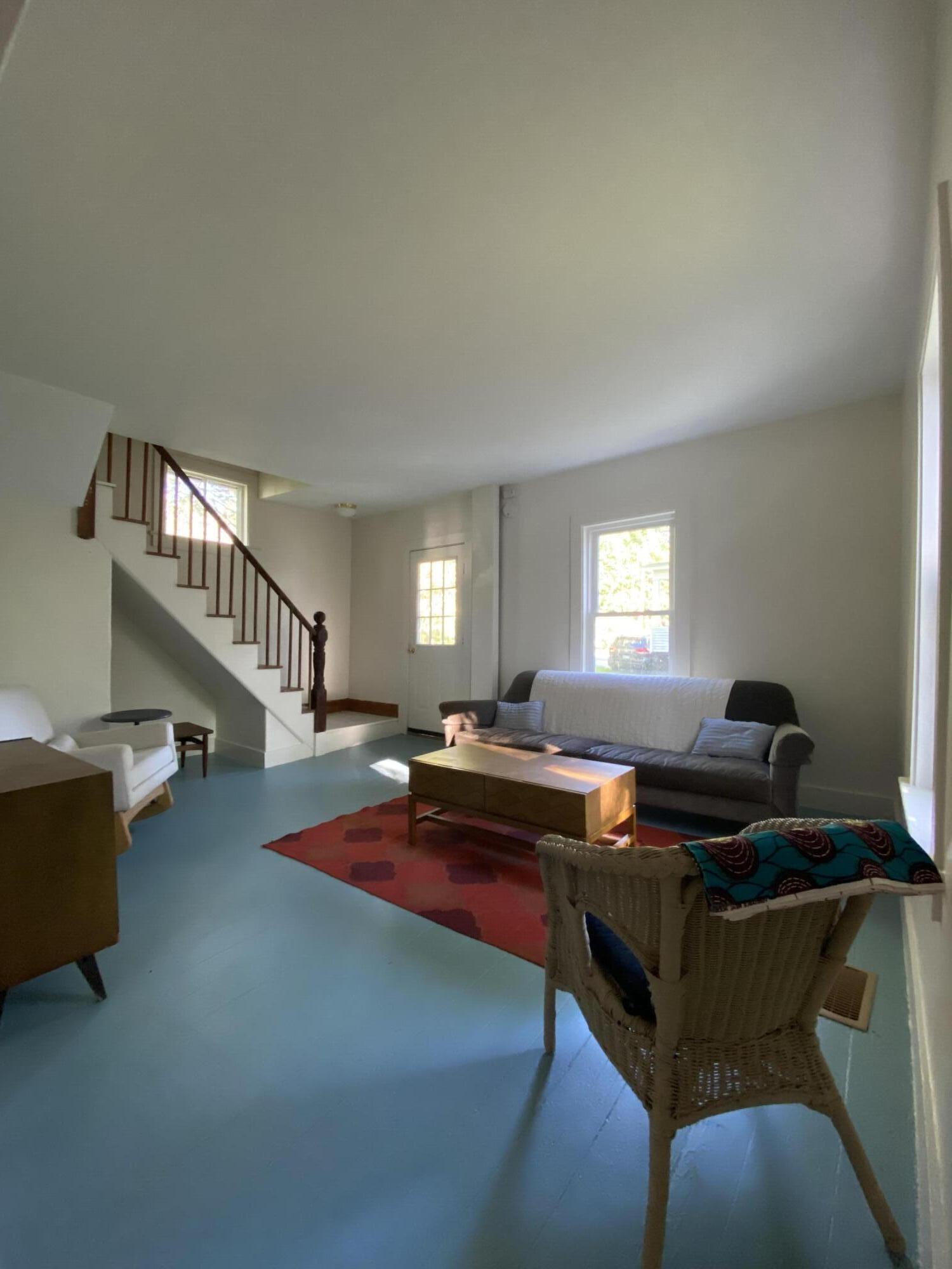 Living room with blue-painted floors, a gray sofa, red rug, and staircase.