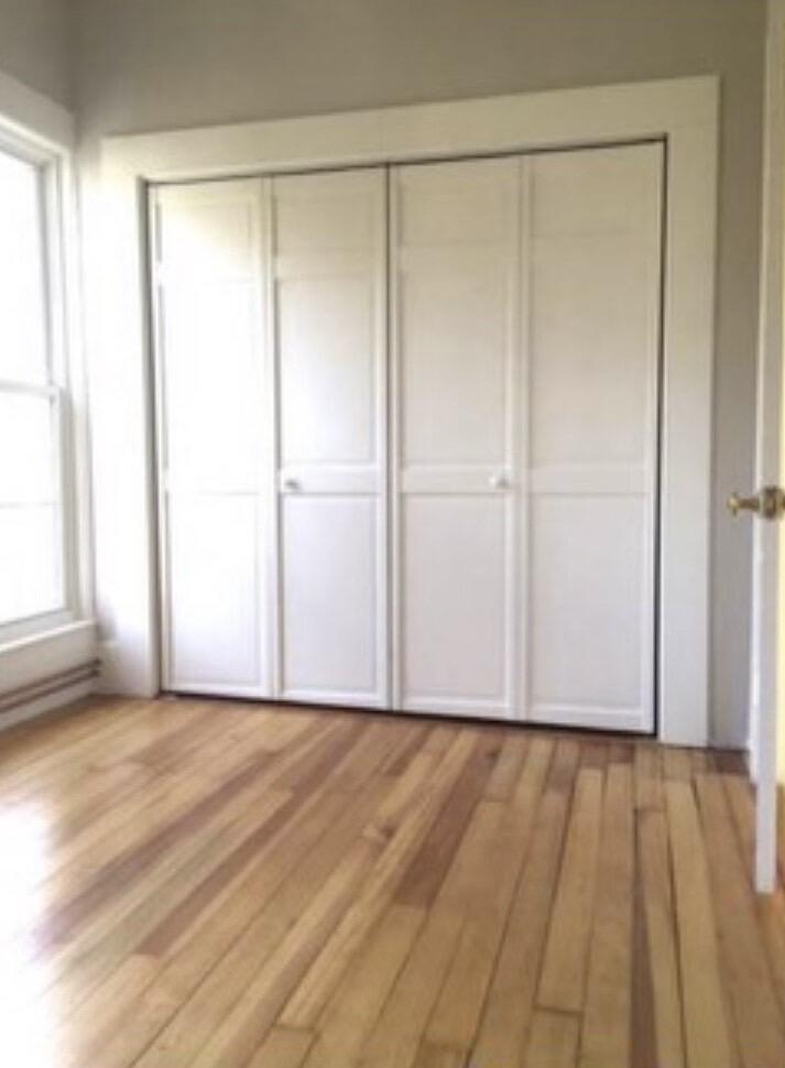 Vacant bedroom with a wide sliding-door closet, large window, and hardwood floors.