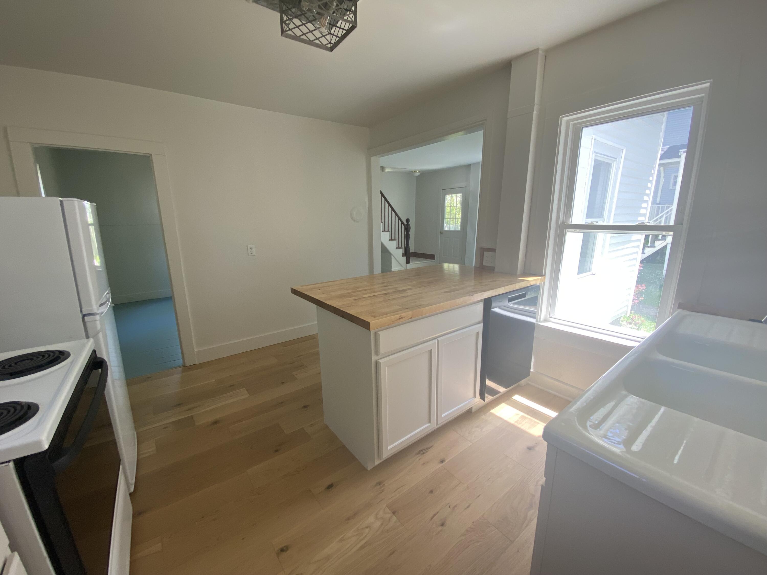Kitchen with a butcher-block island, light wood floors, and a large sunlit window.