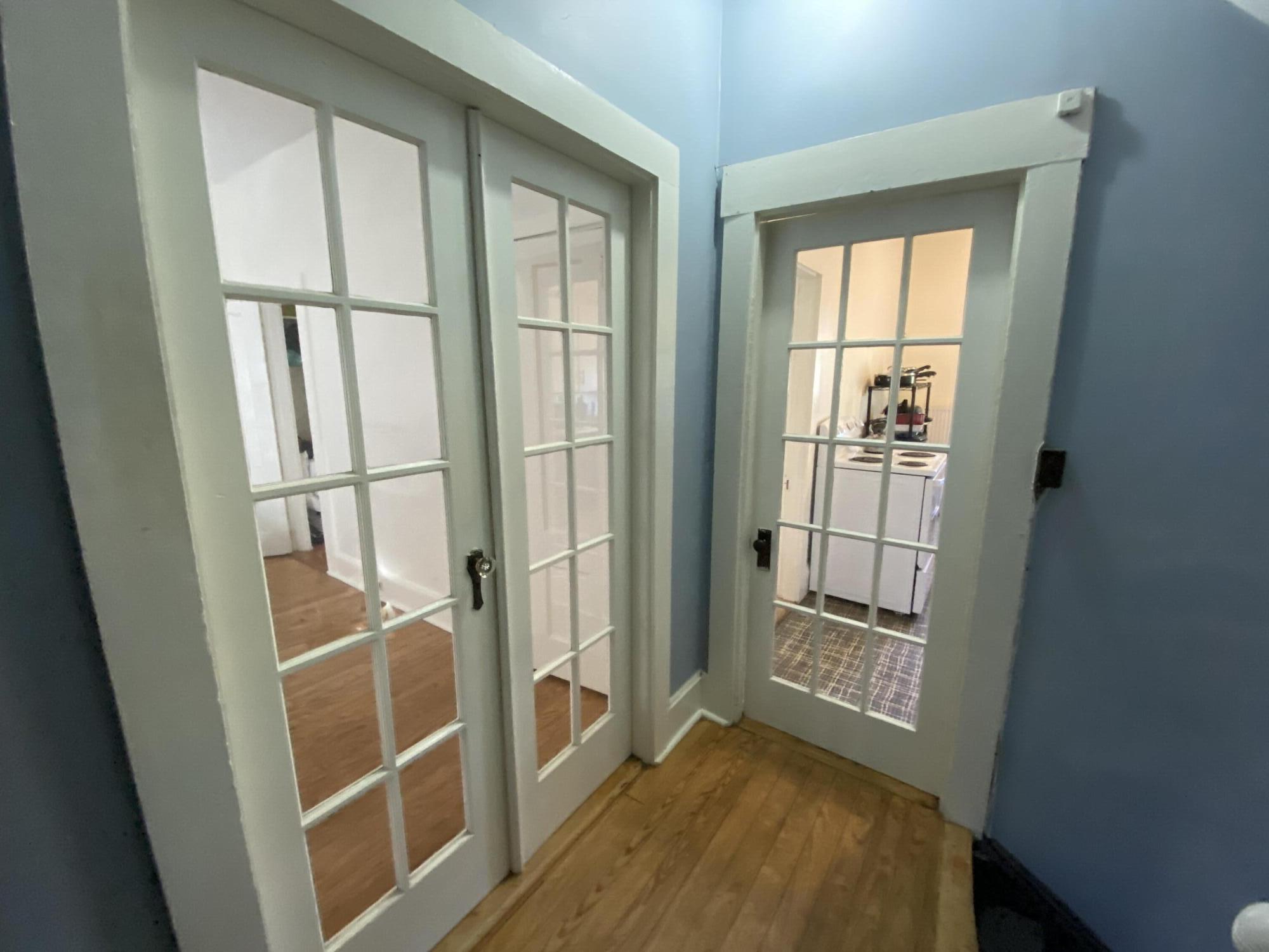 Hallway with hardwood floors and glass-paneled doors opening toward a small kitchen.