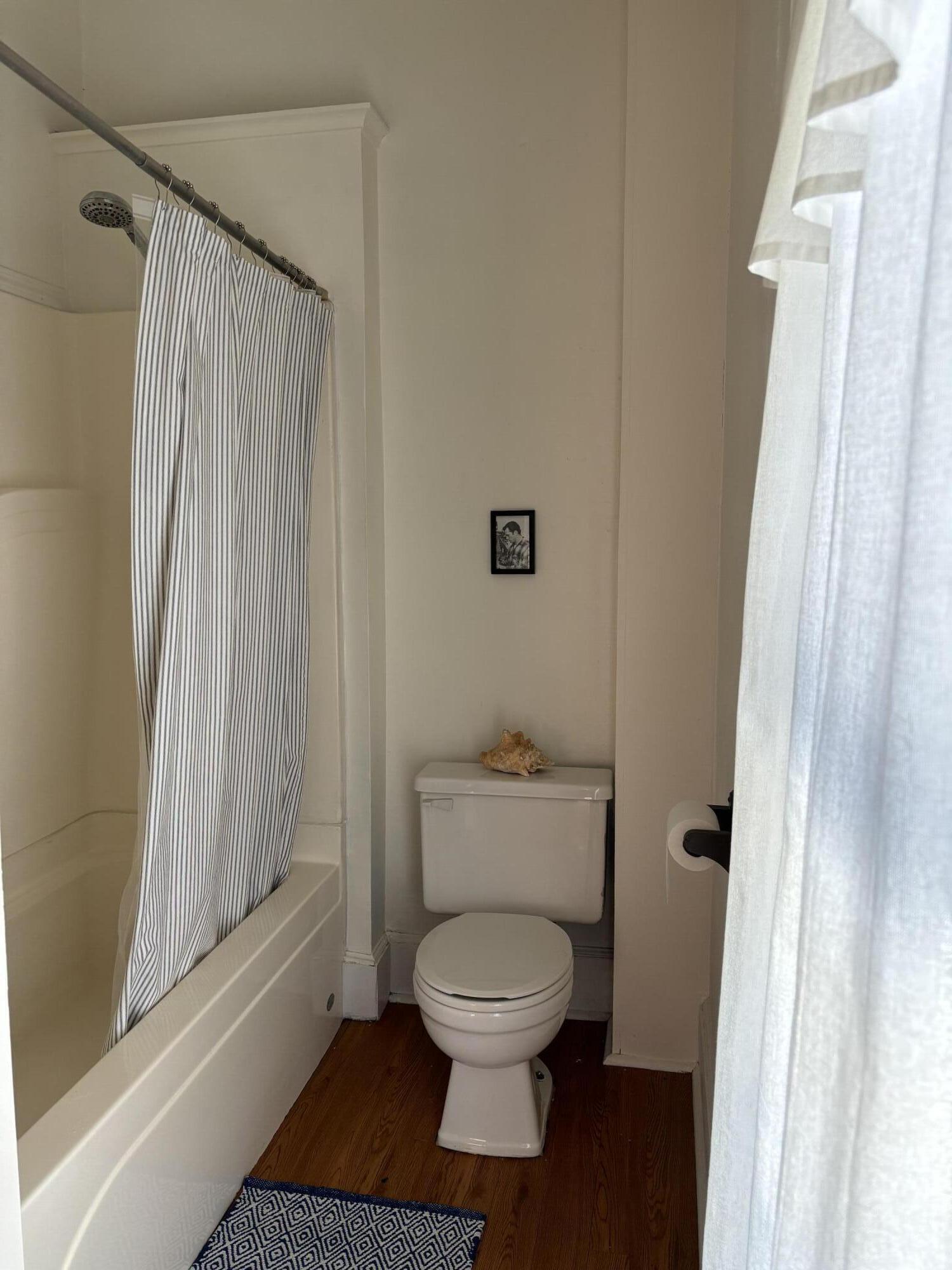 Bathroom with a striped shower curtain, white tub, toilet, and dark wood floor.