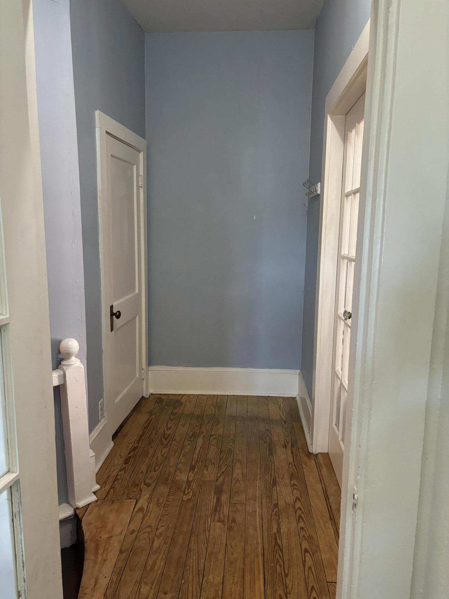 Narrow hallway with hardwood floors, blue-gray walls, and white paneled doors.
