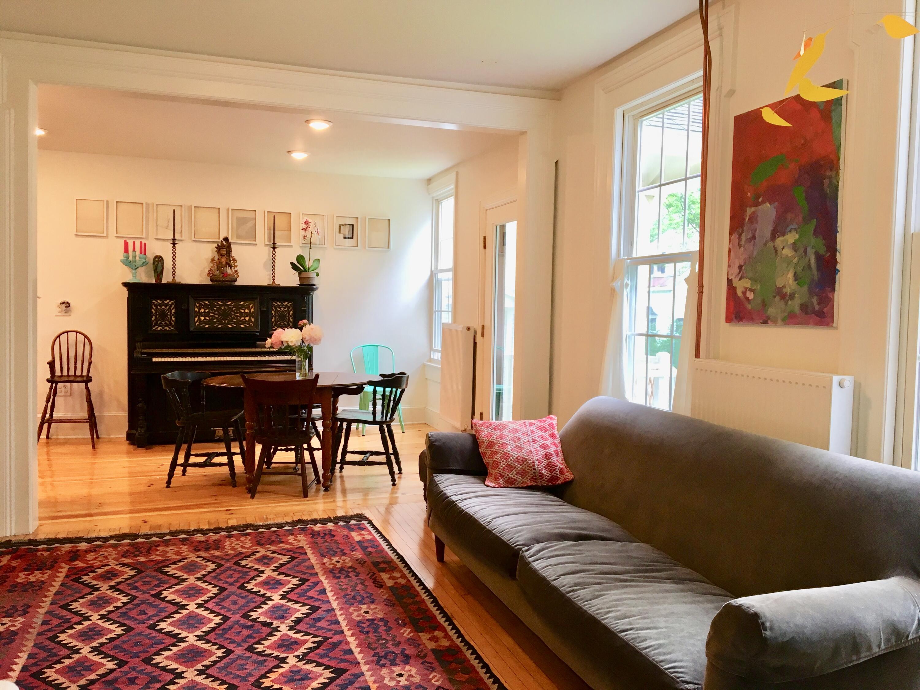 Living room and dining area with a gray sofa, patterned rug, and ornate upright piano.