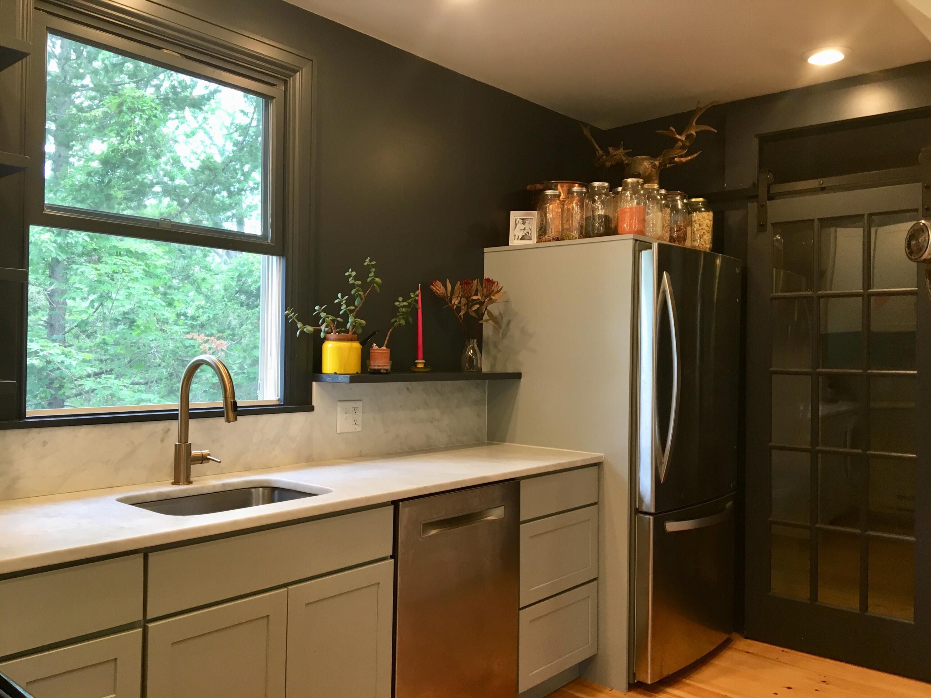 Kitchen with pale paneled cabinets, a large leafy-view window, stainless-steel appliances, and a black barn door.