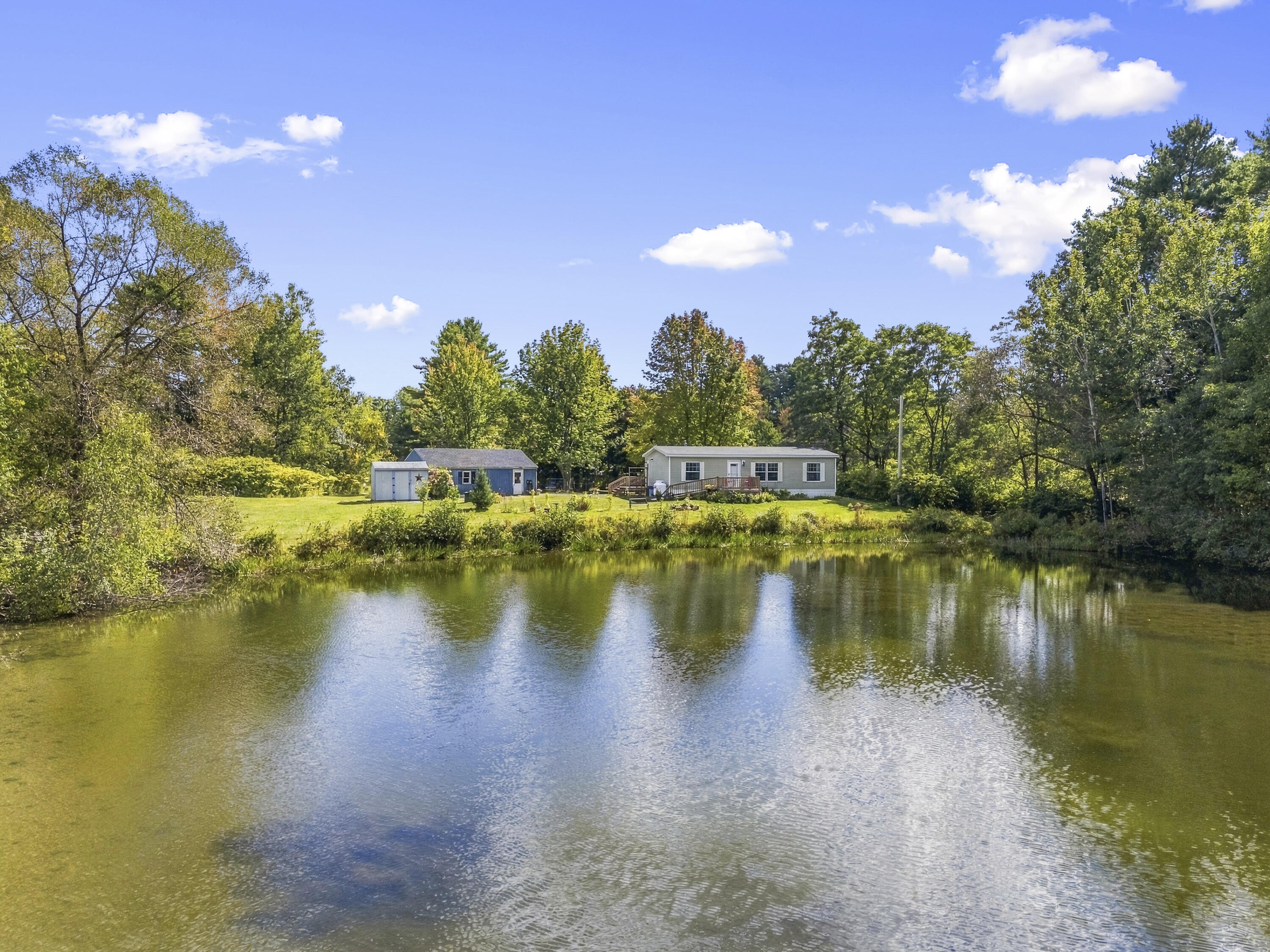Single-story home across a pond, with a detached outbuilding and wooded grounds.
