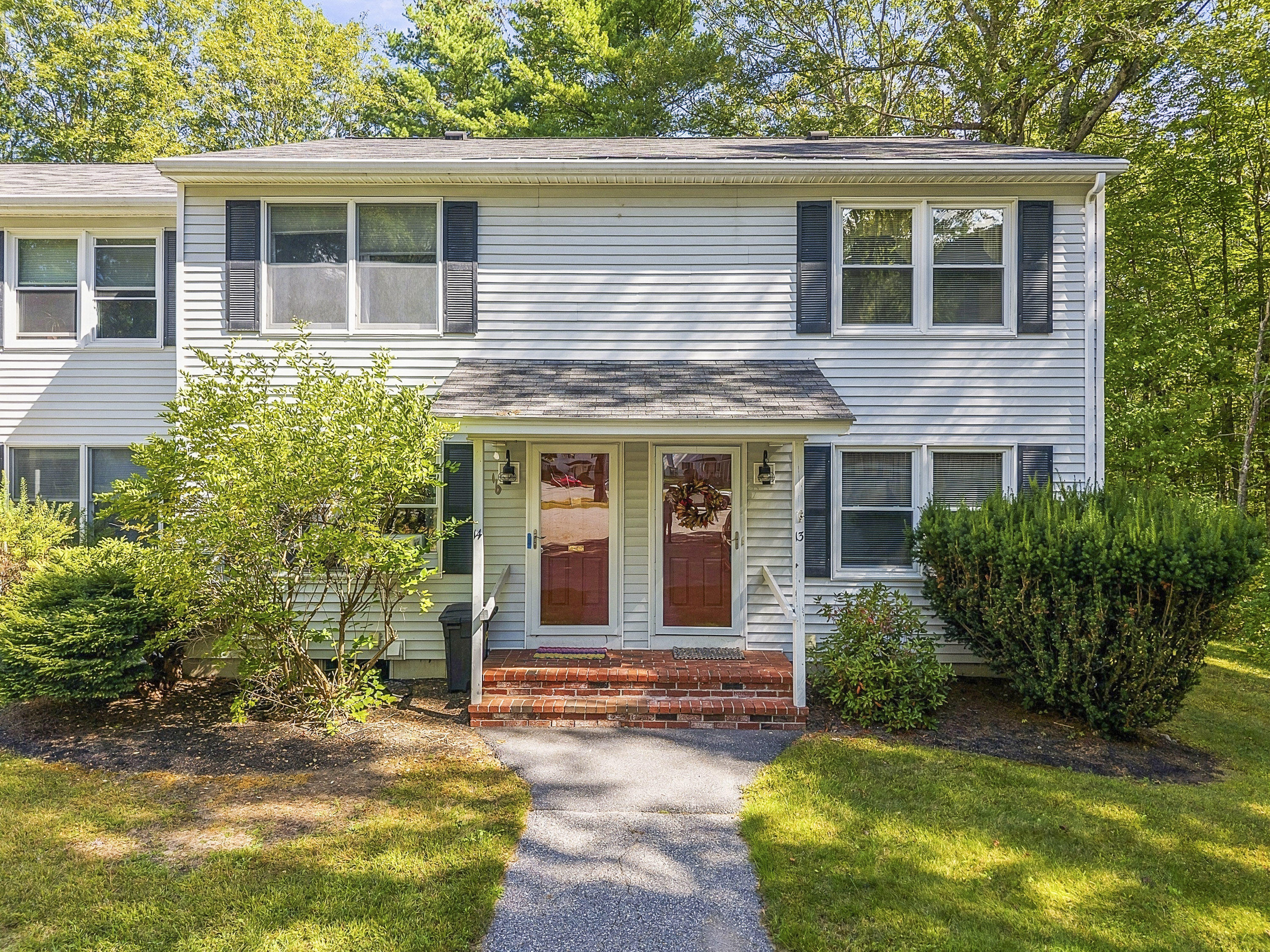 Light-colored duplex with two red front doors, brick steps, and a leafy front yard.