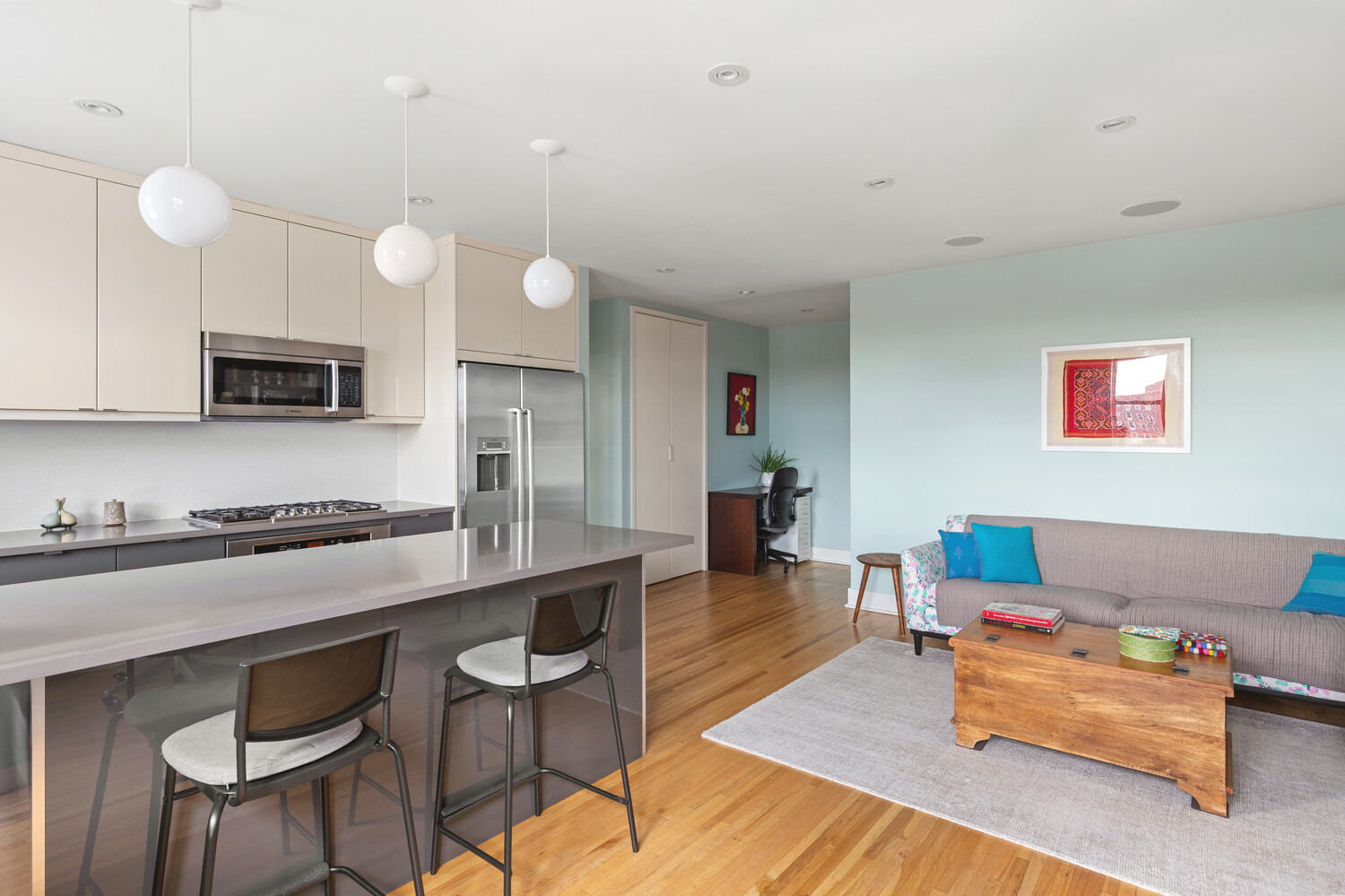 Open-plan kitchen and living room with a wide breakfast bar and gray sofa.