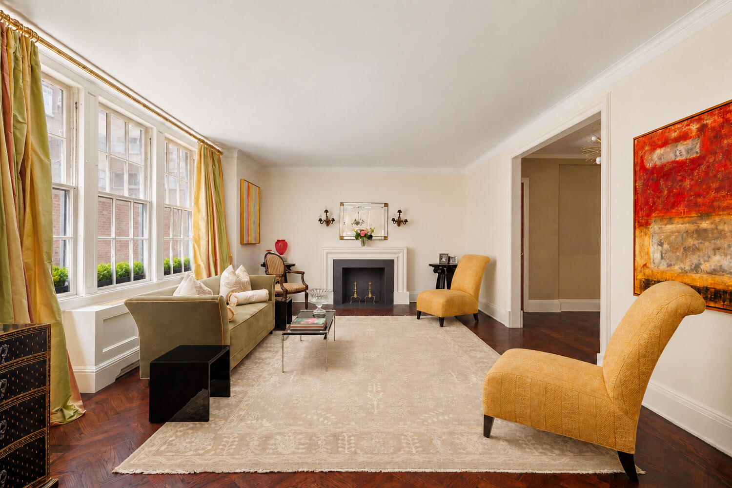 Furnished living room with tall windows, a fireplace, mustard-yellow chairs, and a large cream rug.