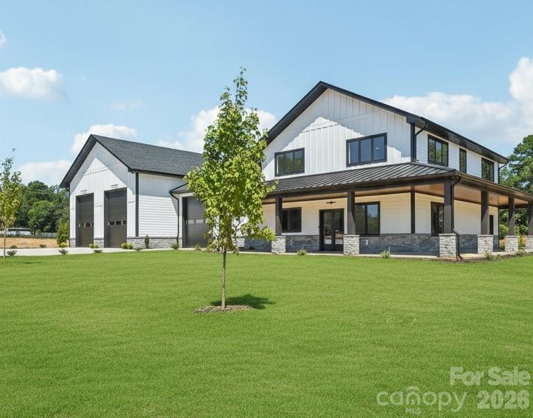 Modern white two-story house with black trim, a covered porch, detached garage, and broad green lawn.