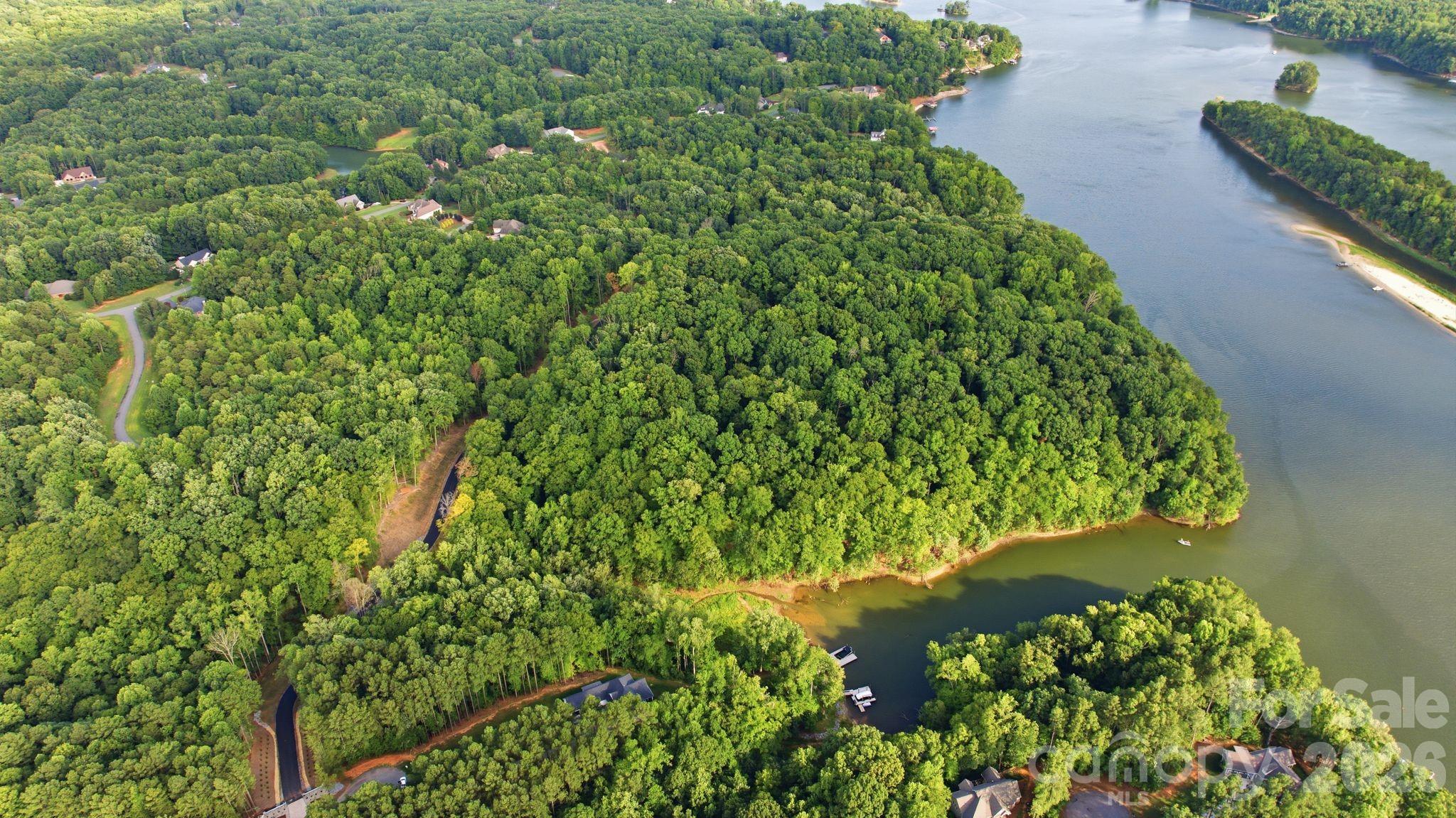 Aerial view of a wooded lakeside peninsula with scattered homes and a sandy shoreline.