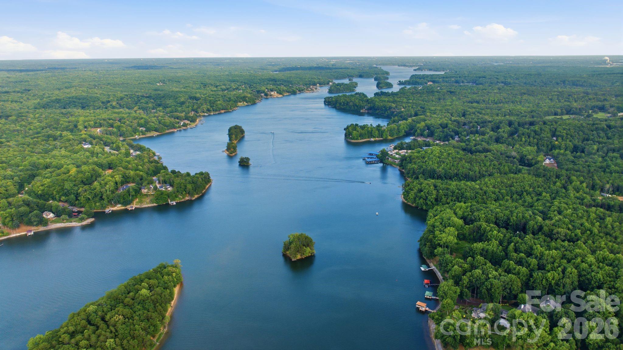 Aerial view of a winding lake bordered by dense green woods, with small islands and homes along the shore.