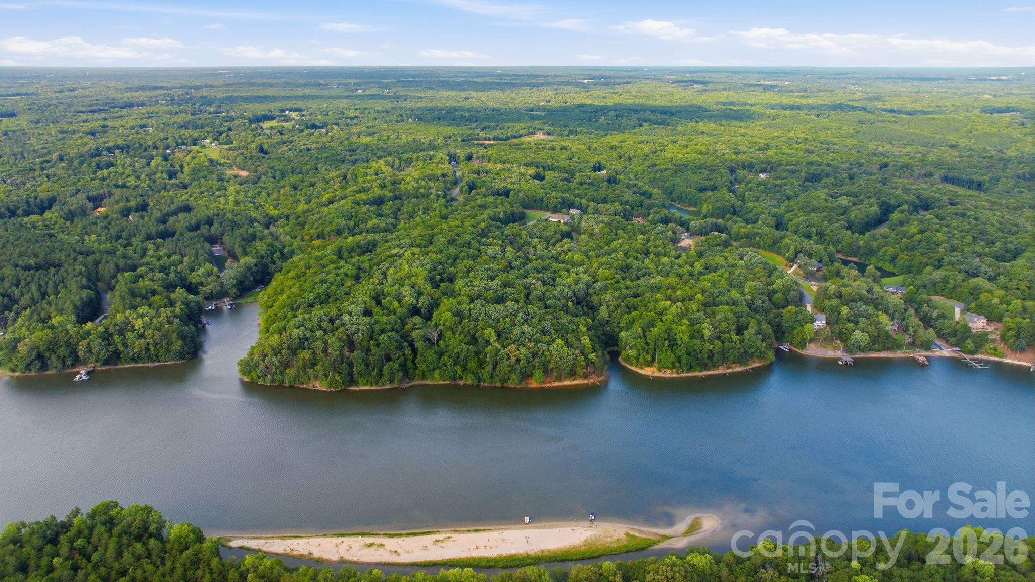 Aerial view of a wooded lake shoreline with scattered homes, docks, and a sandy point.