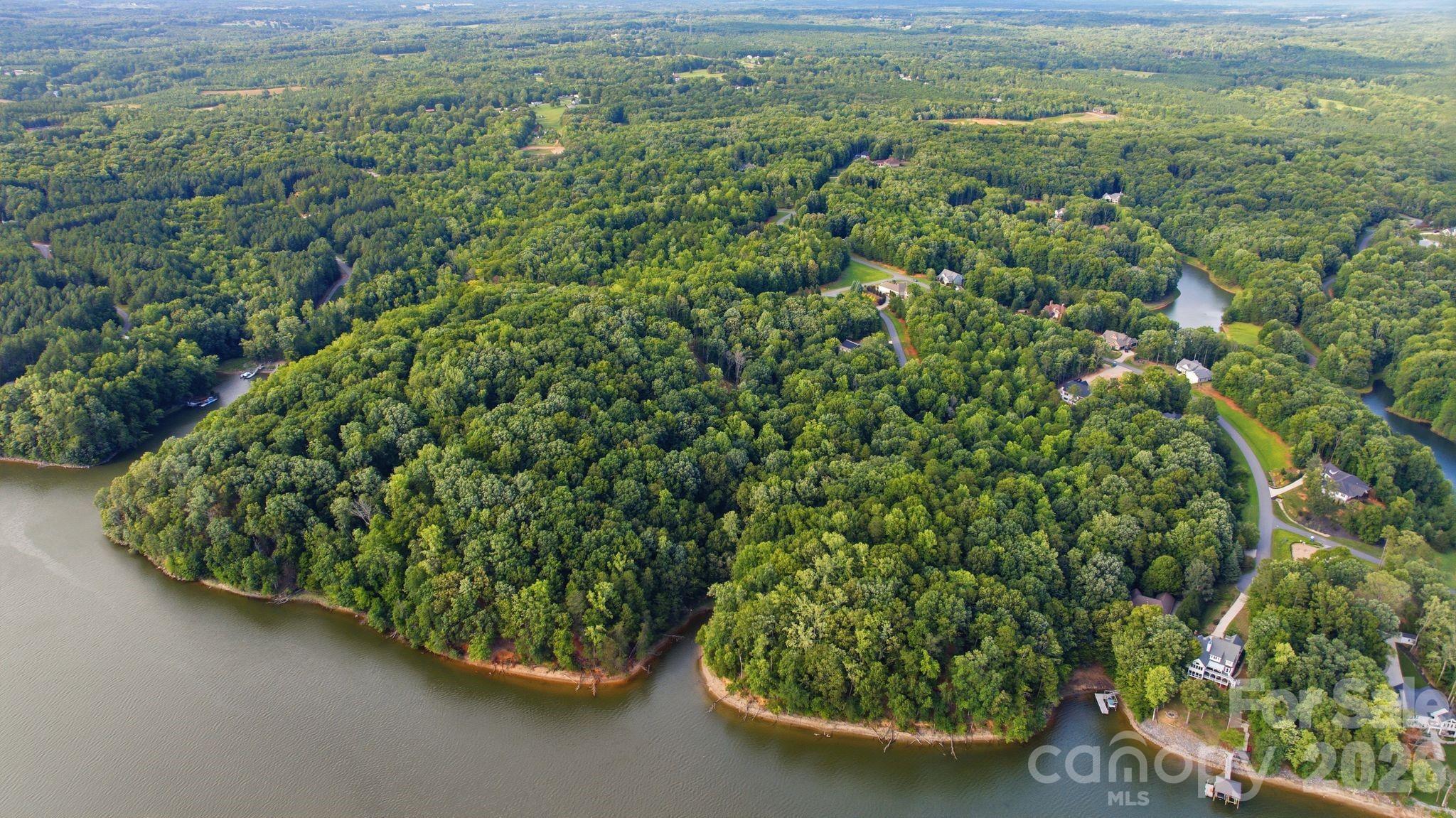 Aerial view of a wooded waterfront neighborhood with homes, winding roads, and coves.