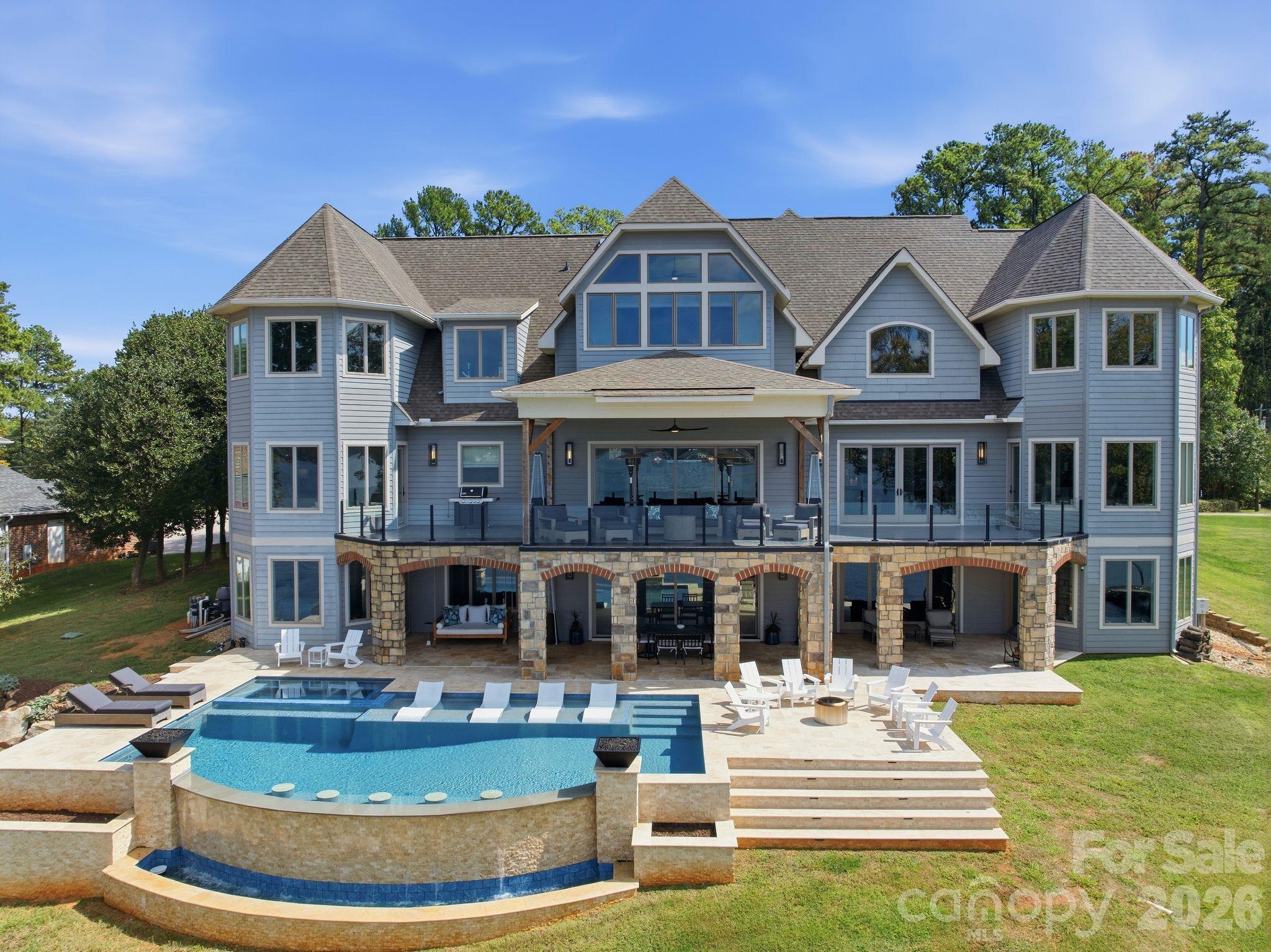 Large gray house with a stone-column patio overlooking a pool and raised spa.