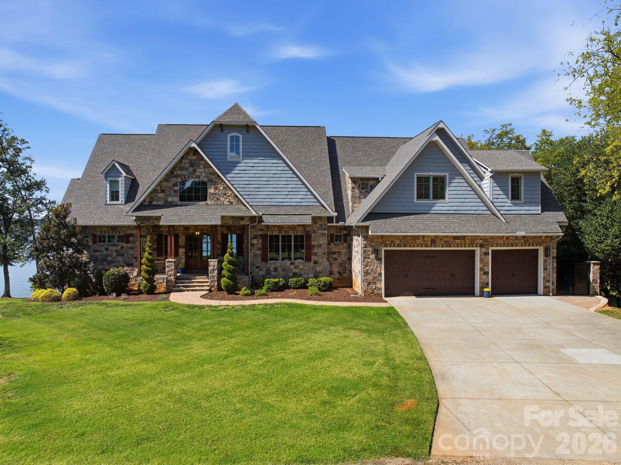 Stone-and-blue-sided home with multiple gables, a three-car garage, and a glimpse of lake water.