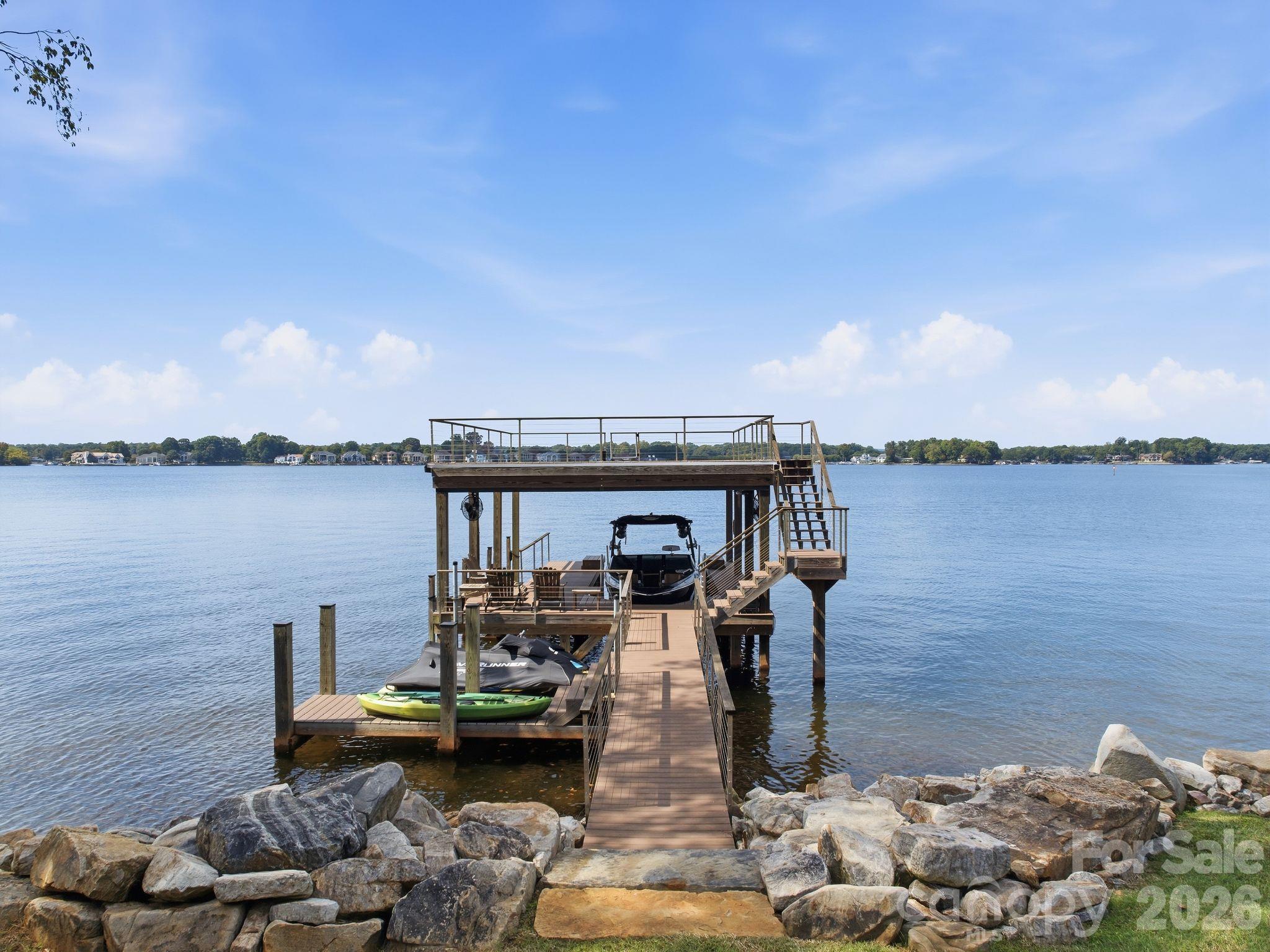 Multi-level wooden dock with a boat and kayak extending into a calm lake.