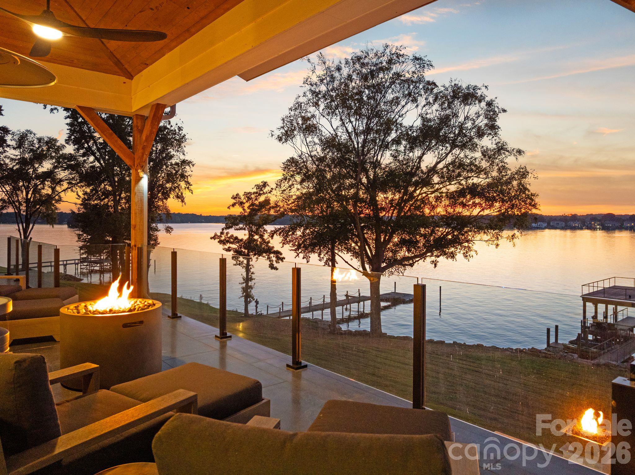 Covered lakeside patio with cushioned seating and fire features overlooking the water at sunset.