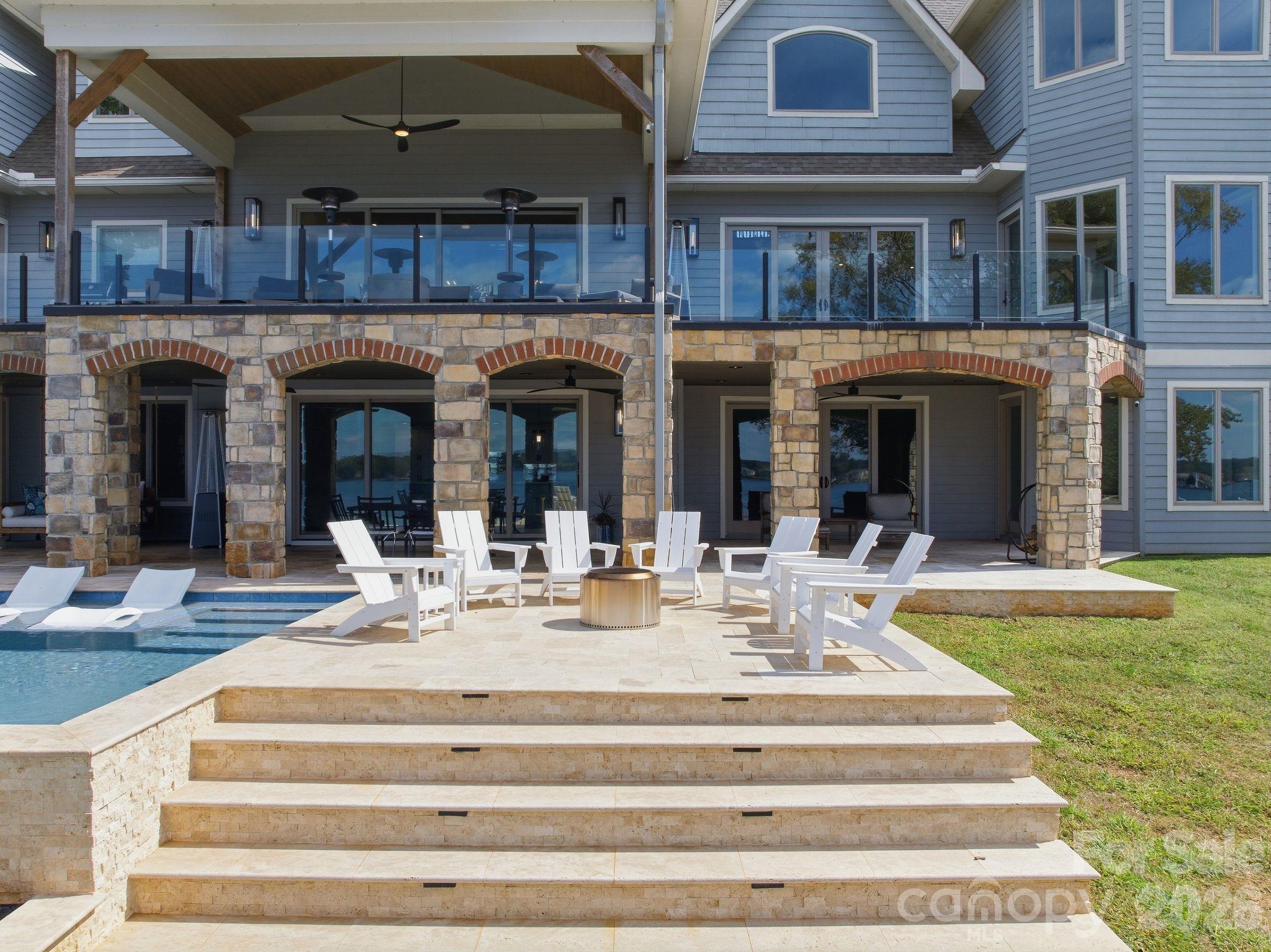 Home’s stone terrace with white lounge chairs and a pool beside the covered patio.