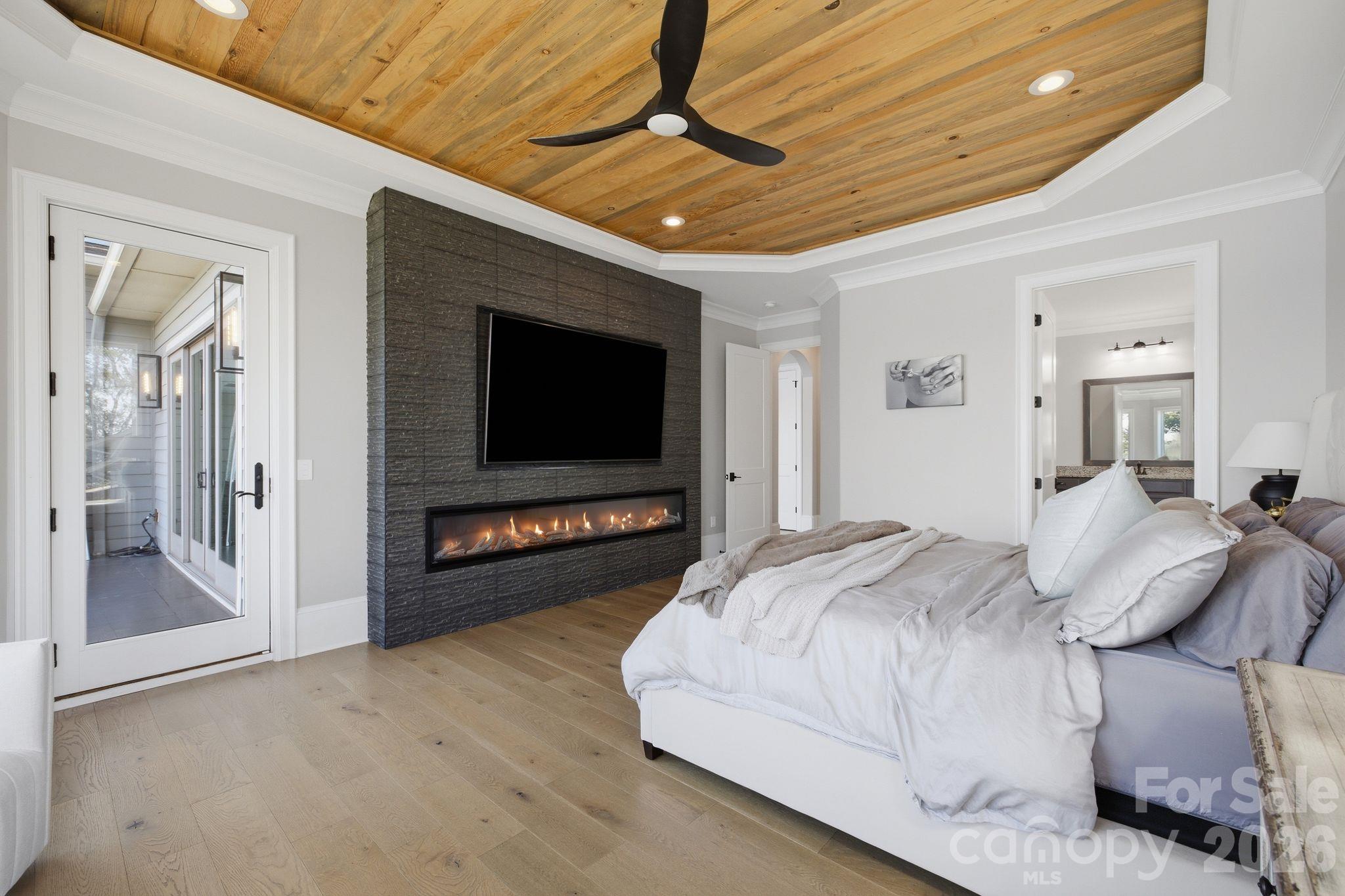 Bedroom with a wood plank ceiling and a television above a long stone-wall fireplace.