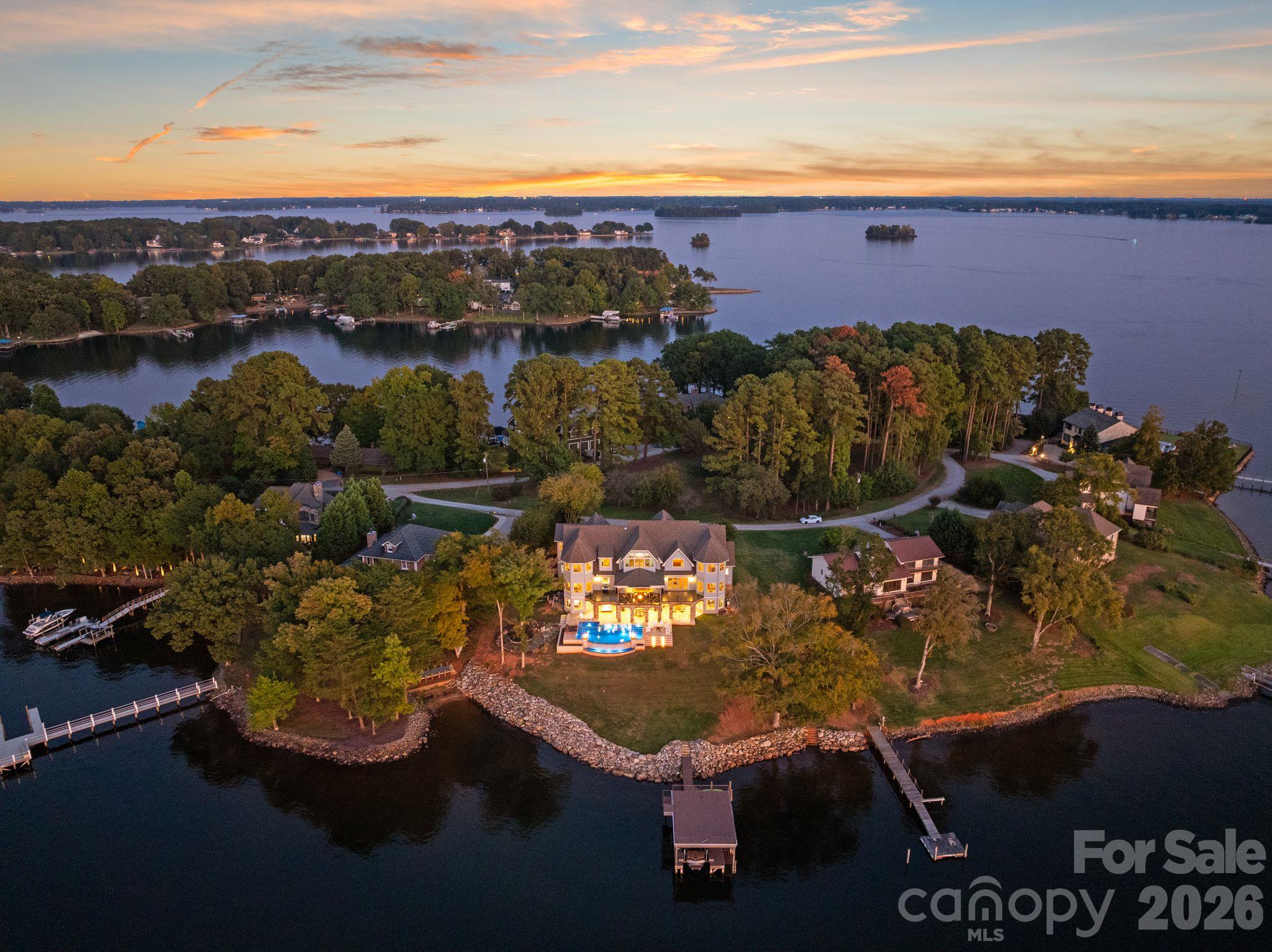 Waterfront home on a wooded peninsula, with a lit pool, multiple docks, and lake views at dusk.