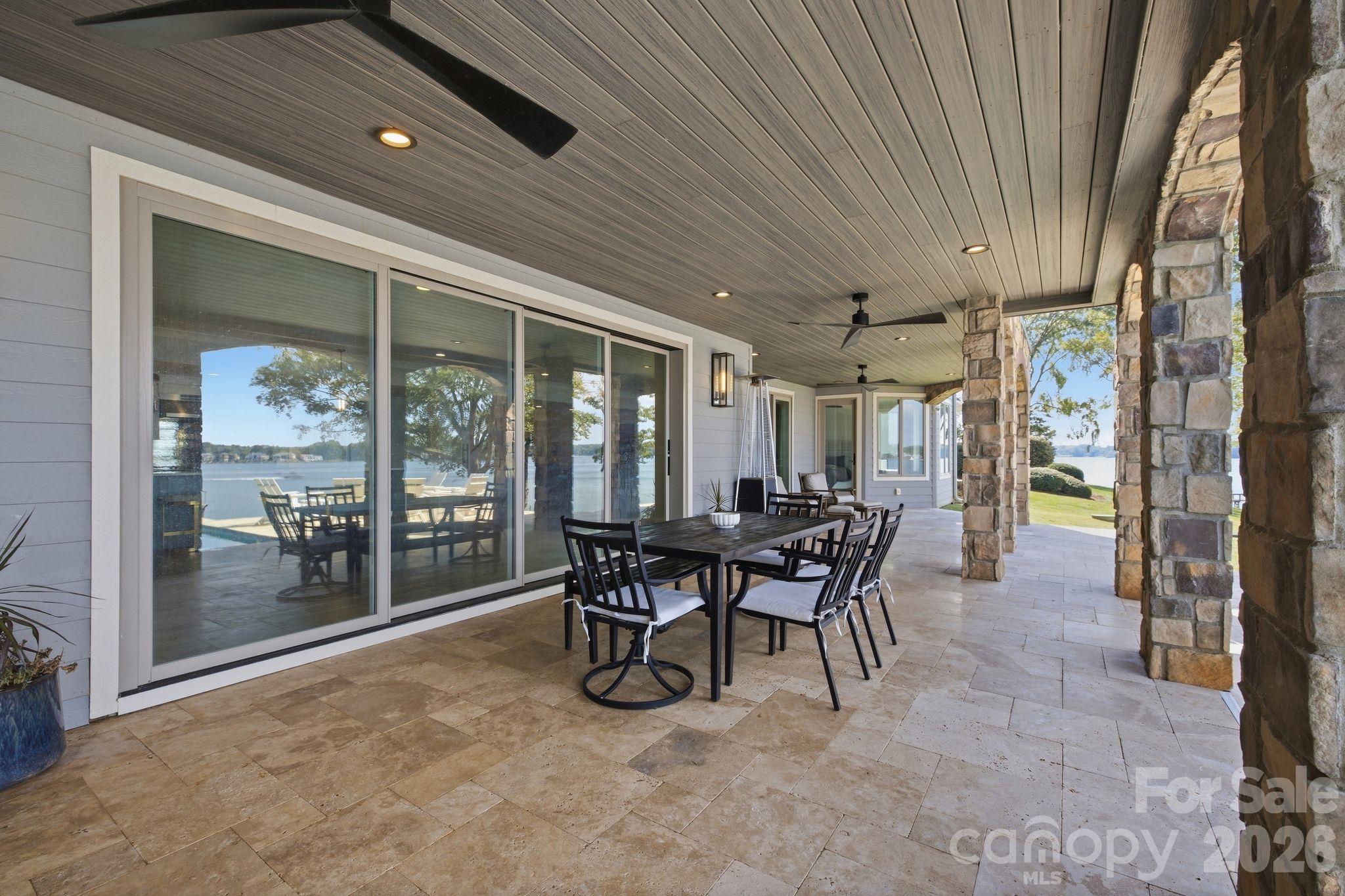 Covered lakeside patio with stone columns, outdoor dining set, and views of the water.