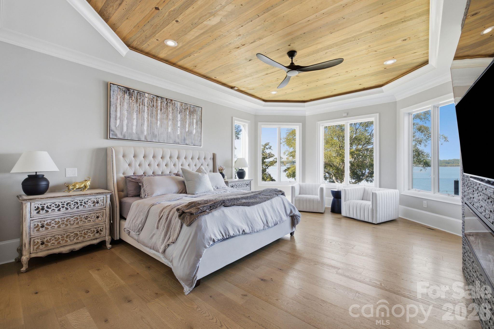 Furnished bedroom with a wood-plank ceiling, lake-view windows, and a large upholstered bed.